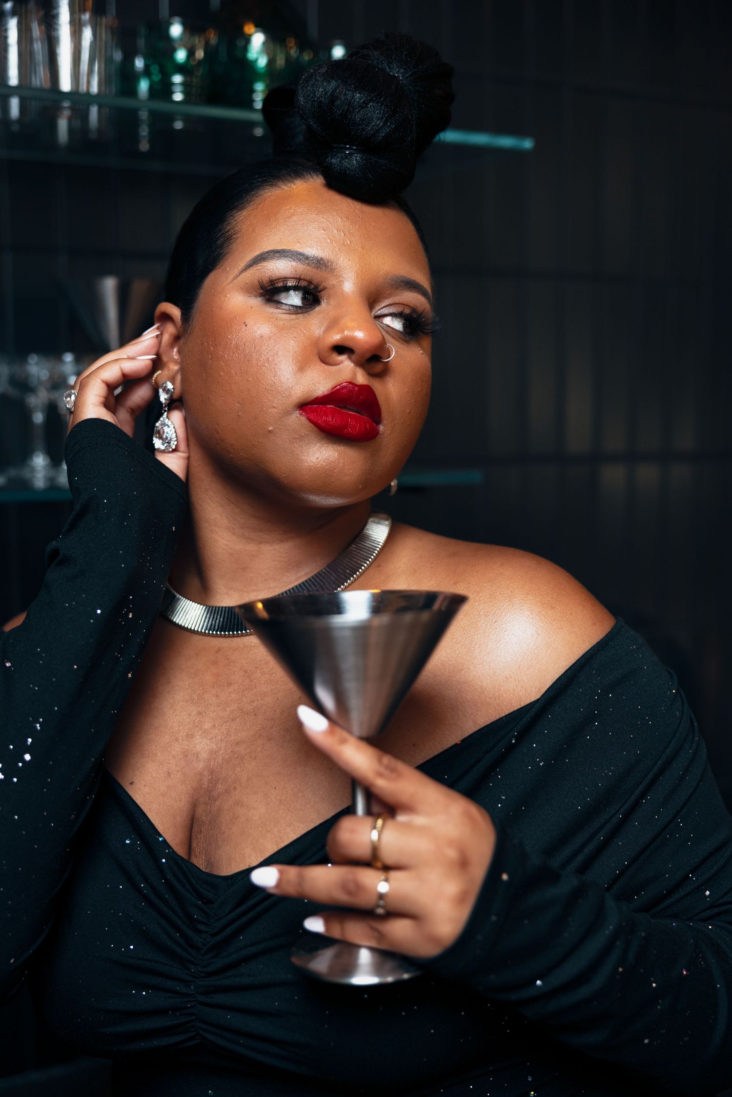 Glamorous plus-size woman in black sequin off-shoulder dress holds silver cocktail cup with red lips.
