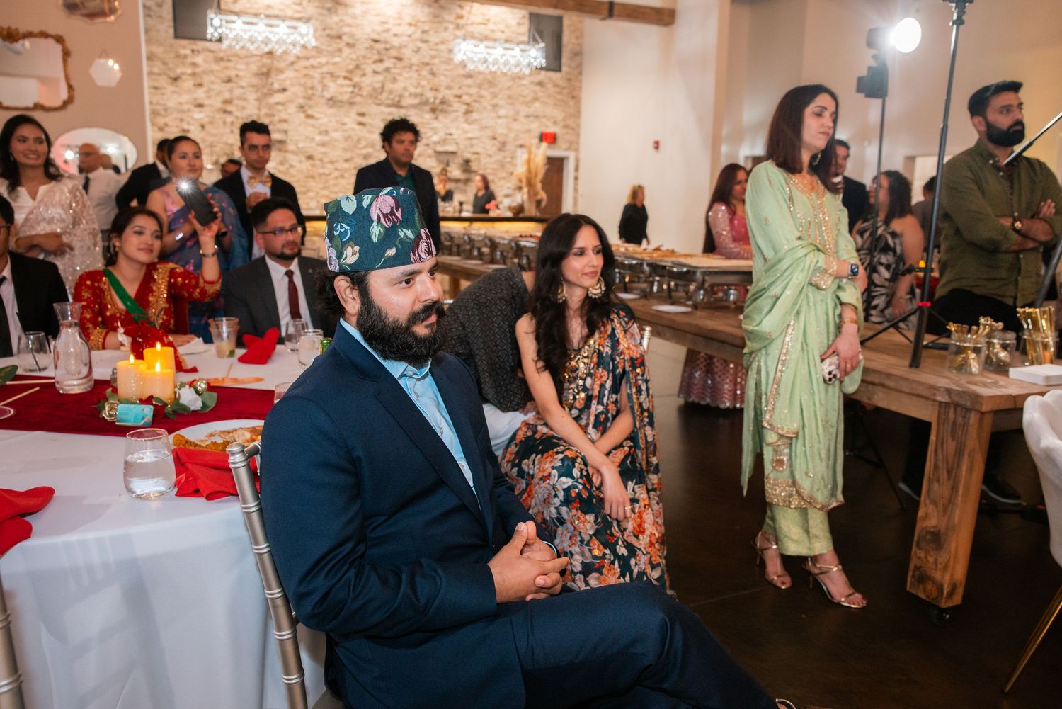 Guests in traditional South Asian attire enjoying wedding reception program.
