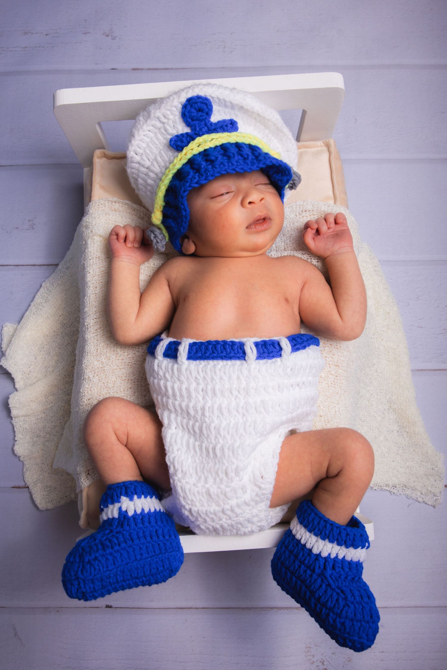 Sleeping newborn baby in crocheted sailor outfit with blue booties on a white bed.