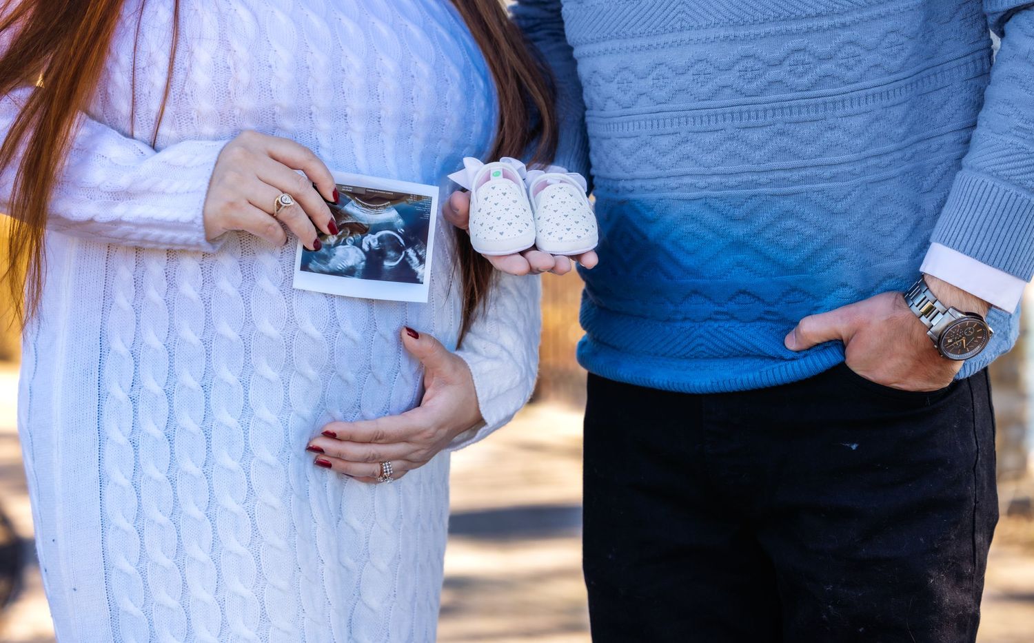 Pregnant couple holding ultrasound photo and baby booties, maternity announcement photo.