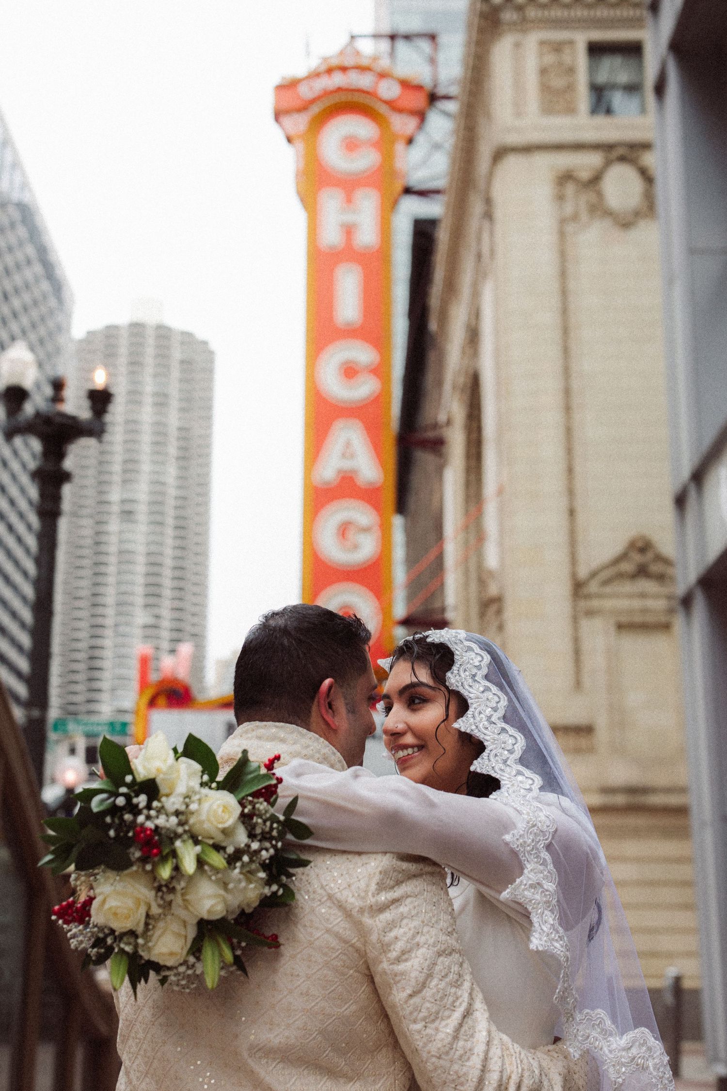 Bride smiles at groom while embracing beneath the vibrant Chicago Theatre sign outdoors.
