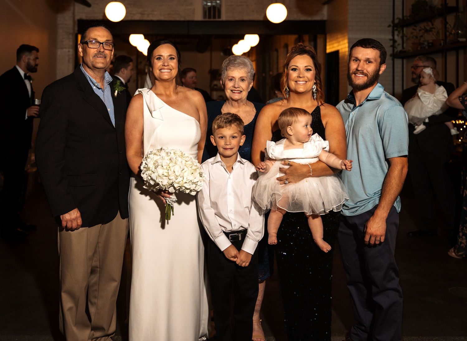 Family portrait with bride holding white bouquet at elegant wedding reception.