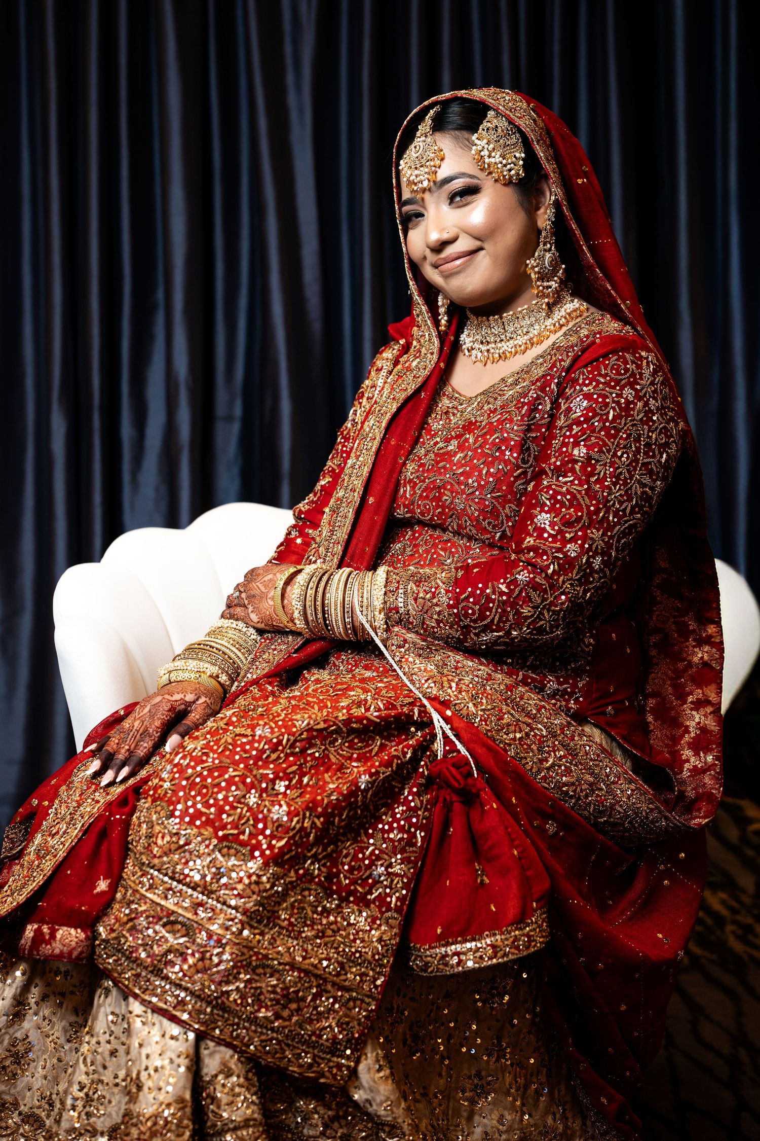 Bride smiling in red and gold embroidered South Asian bridal lehenga with jewelry.