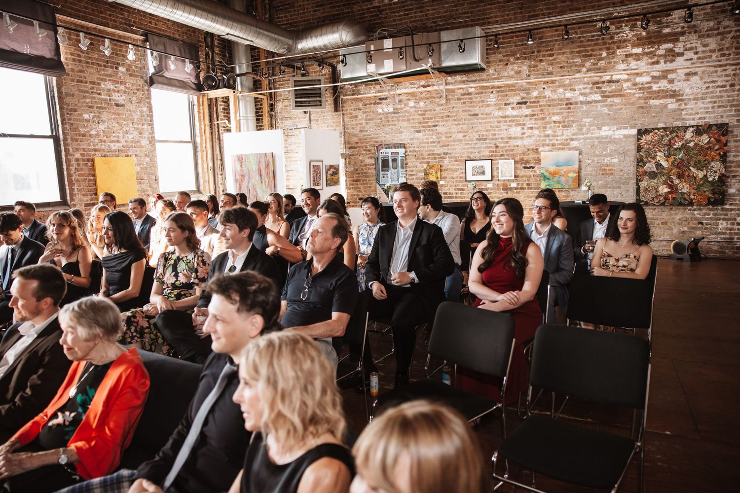 Wedding guests seated in rows in a rustic brick wall art gallery venue.