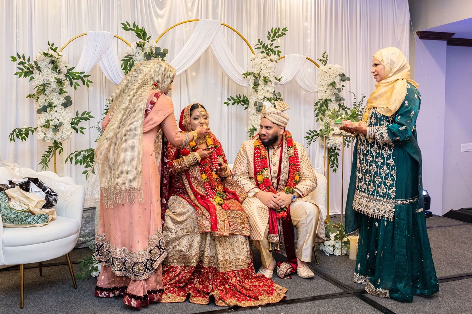 Traditional South Asian wedding ceremony with bride, groom, and guests under floral arch.