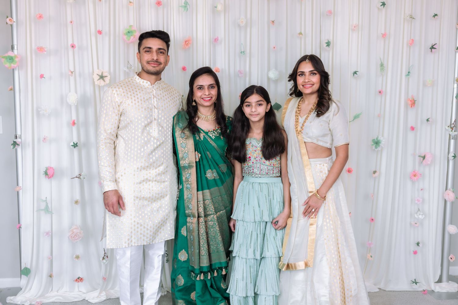 Family of four posing at Indian celebration, including young girl in mint lehenga.