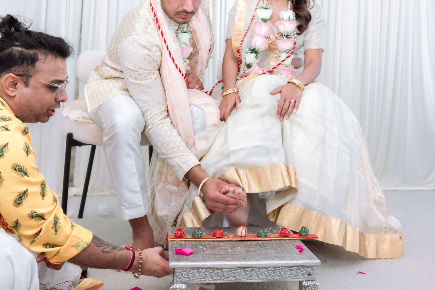 Hindu priest performing traditional foot washing ceremony for Indian bride and groom during wedding.