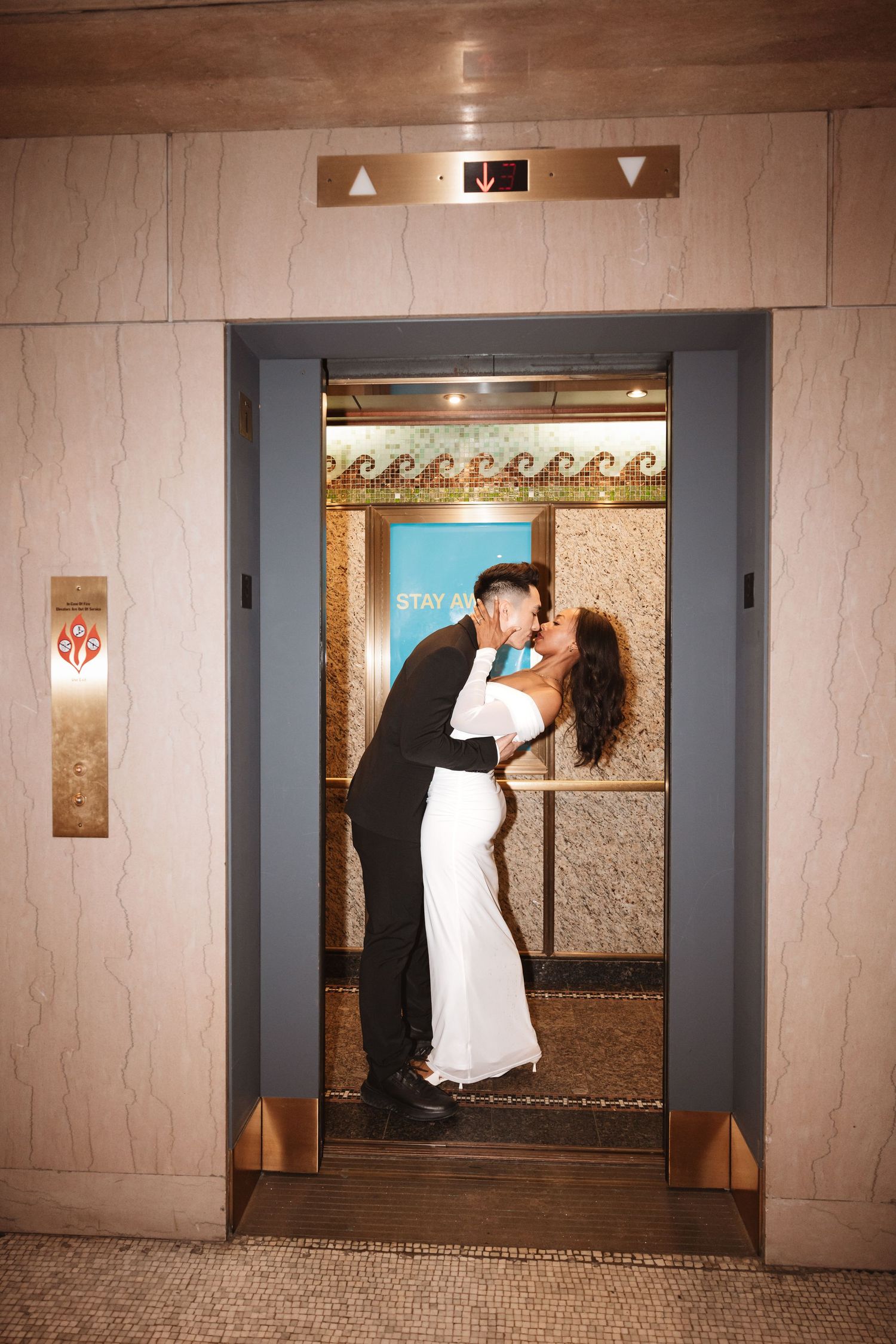 Bride in white gown and groom in black suit kissing in an open elevator doorway.Chicago Wedding Photographer