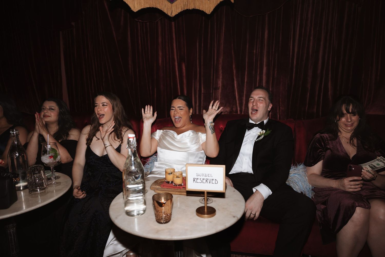 Joyful bride and groom celebrating with wedding guests at a glamorous red velvet reception venue.
