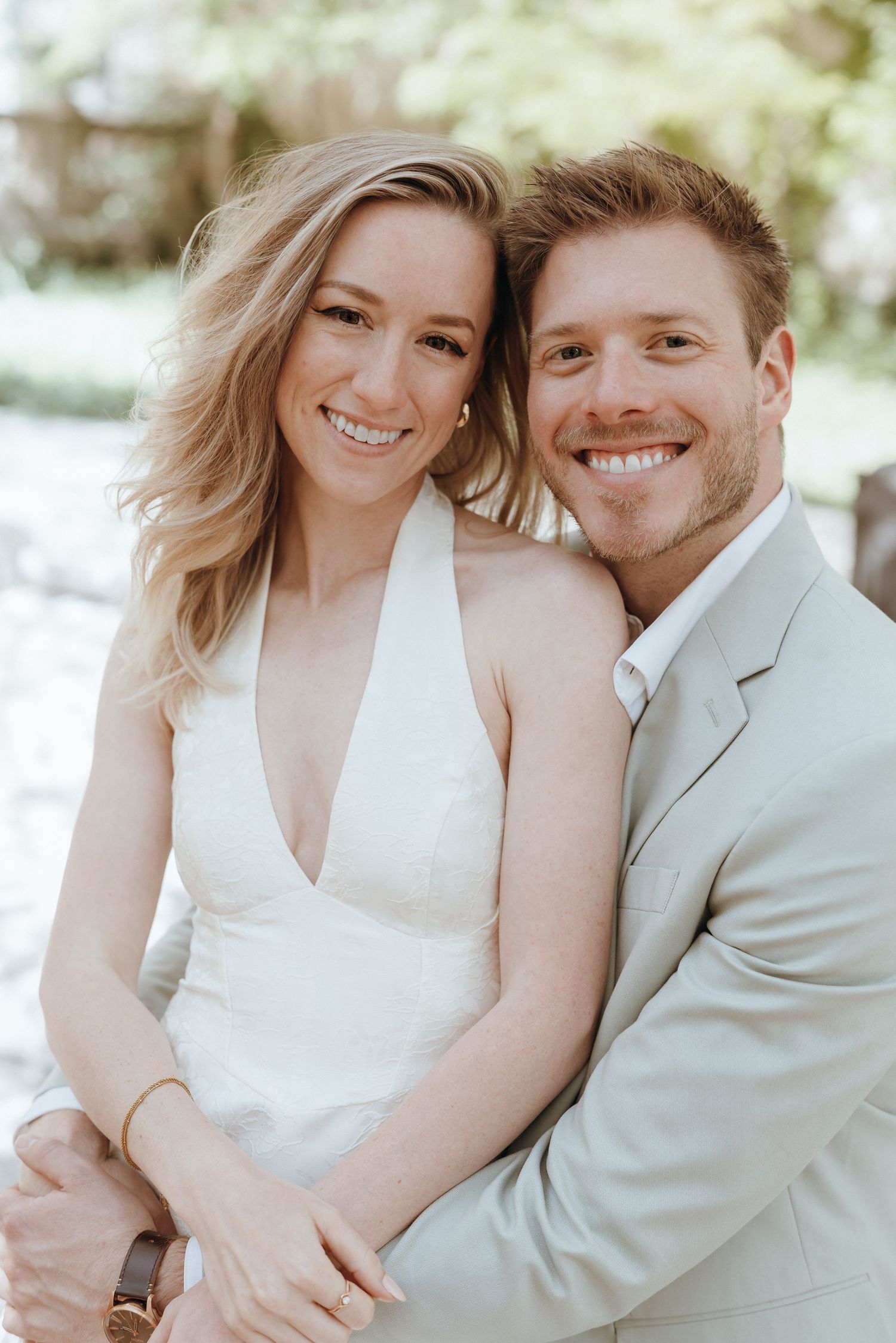 Smiling bride and groom in white halter dress and sage suit pose for outdoor wedding portrait.