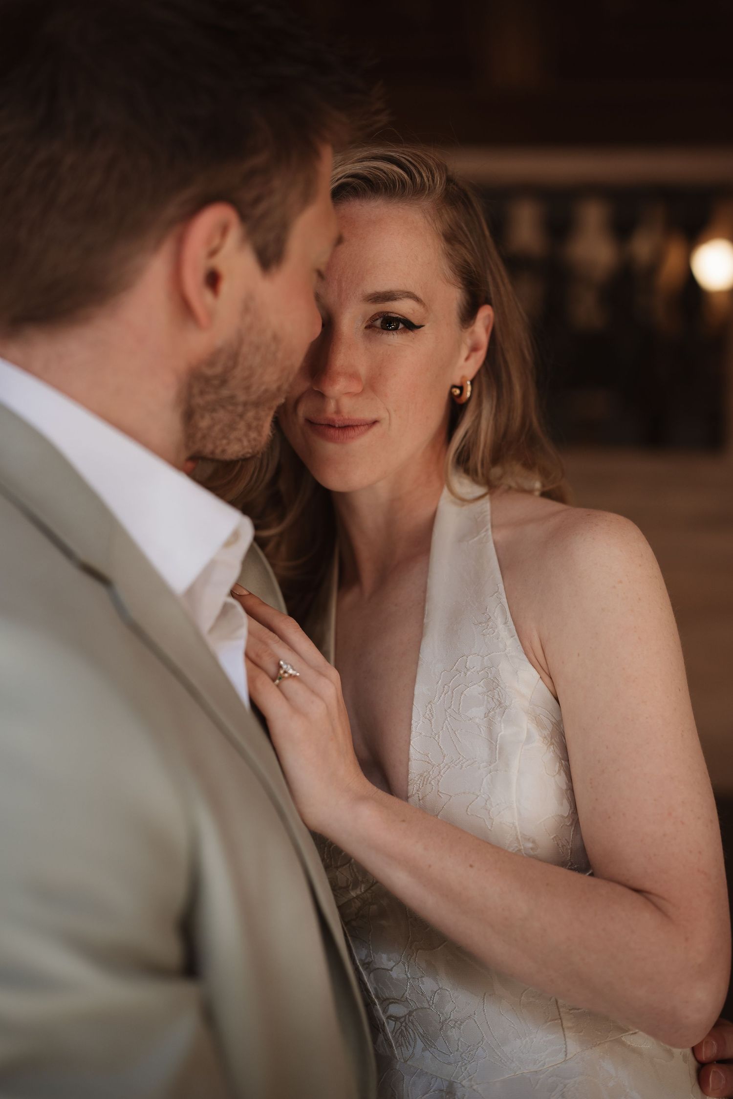Bride in halter wedding dress gazes at groom in sage suit during intimate wedding portrait.