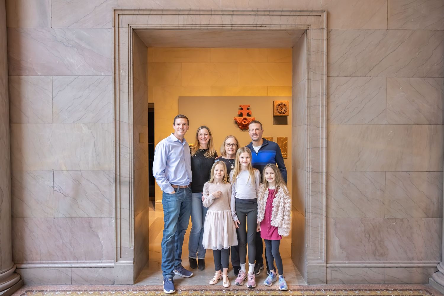 Family of seven posing in an ornate stone archway at a classic building entrance.