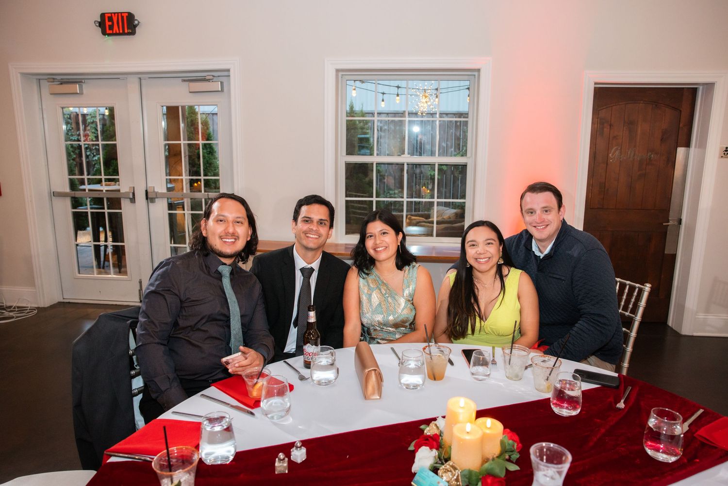 Five wedding guests smile together at decorated table at Indian wedding reception dinner.