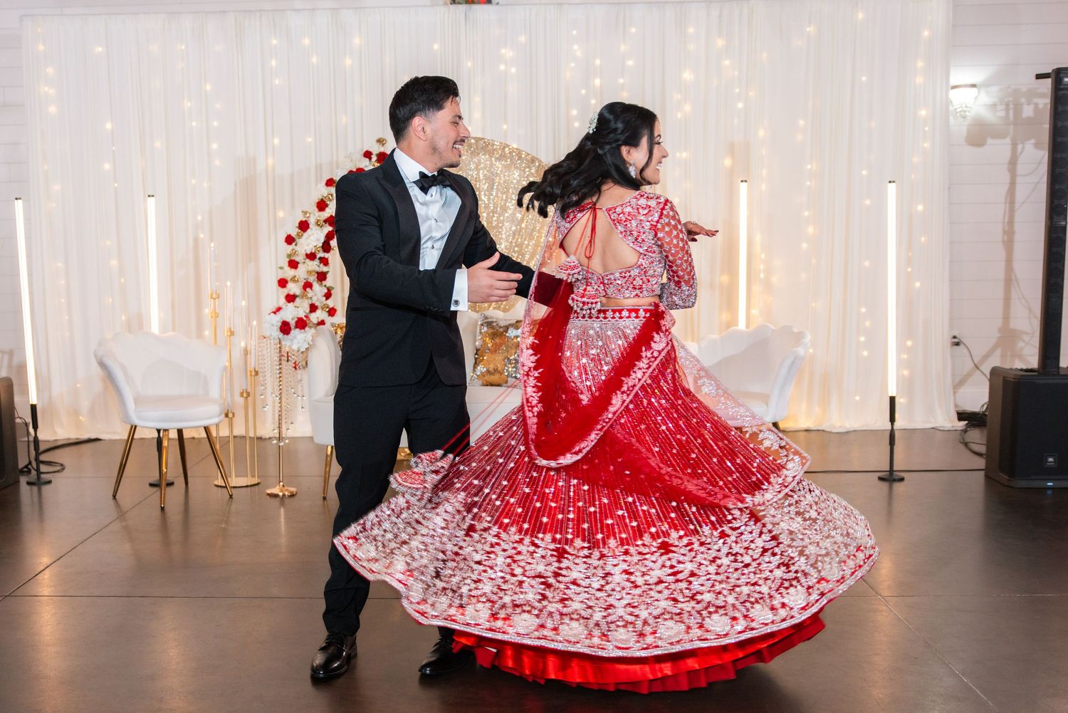 Groom twirling bride in flowing red embroidered lehenga during energetic first dance at Indian wedding.