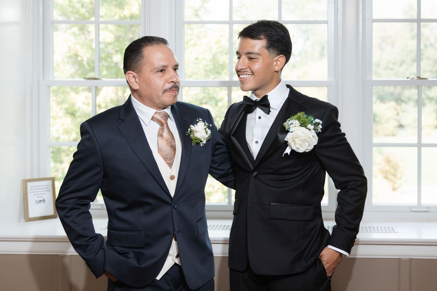 Groom and father smiling together in suits with boutonnieres.