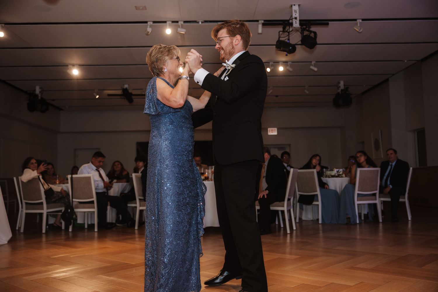 Mother and son sharing a dance at wedding reception in elegant blue gown and tuxedo.