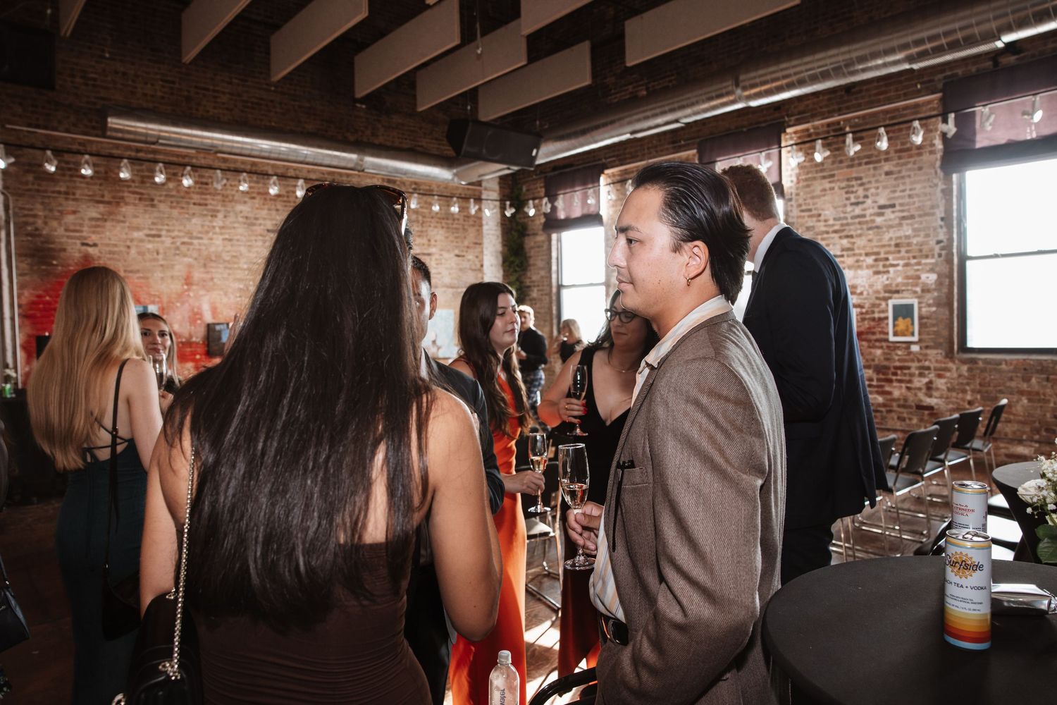 People networking at an indoor bar event in a rustic brick-walled venue.