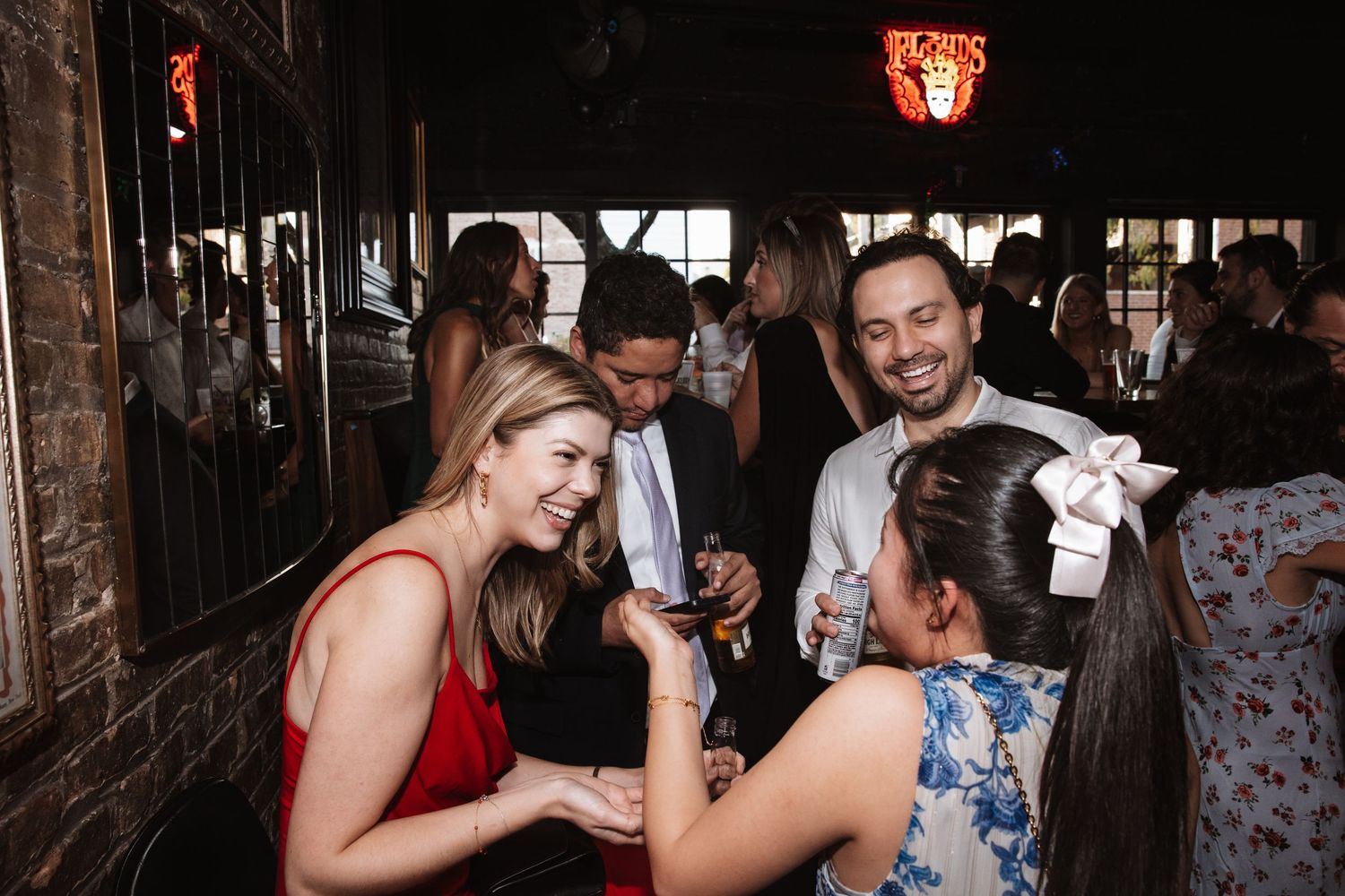 Guests in formal attire laugh and socialize together at an indoor wedding reception venue.