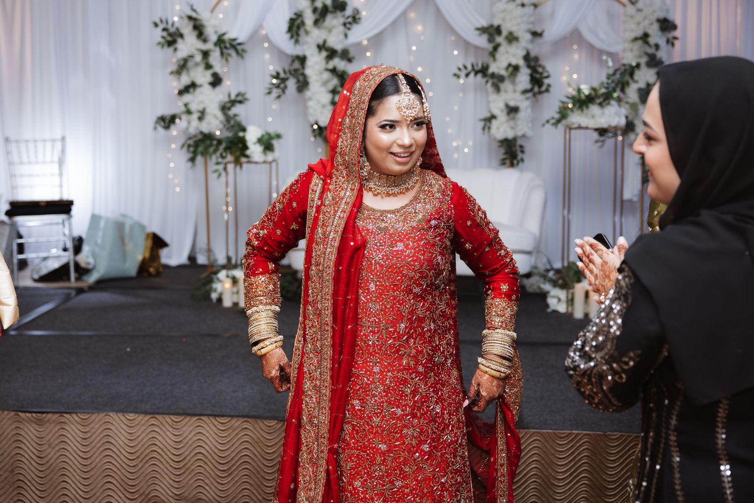 Smiling South Asian bride in red embroidered bridal lehenga and dupatta at wedding reception.