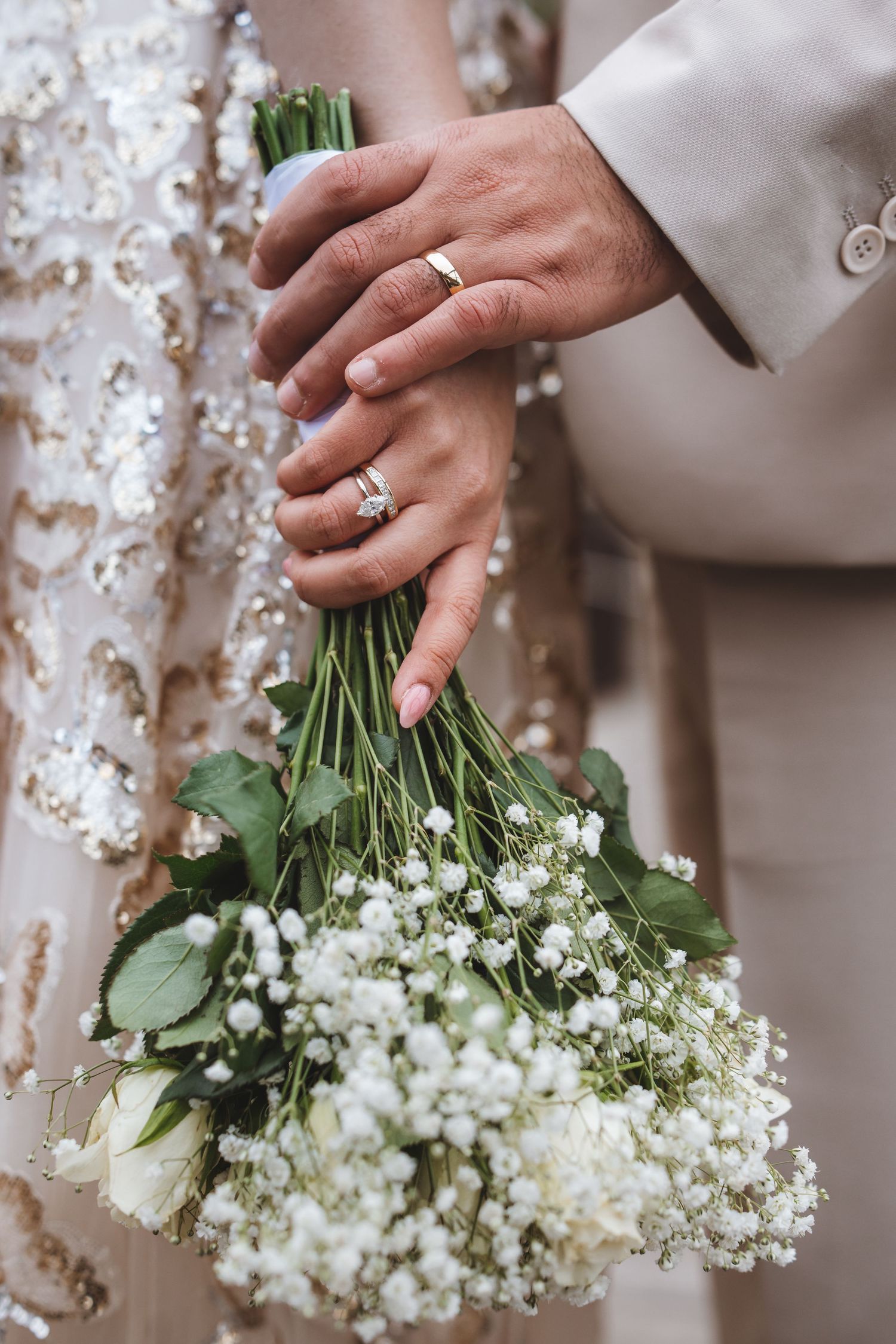 Bride and groom holding white baby's breath wedding bouquet, showing off wedding rings.