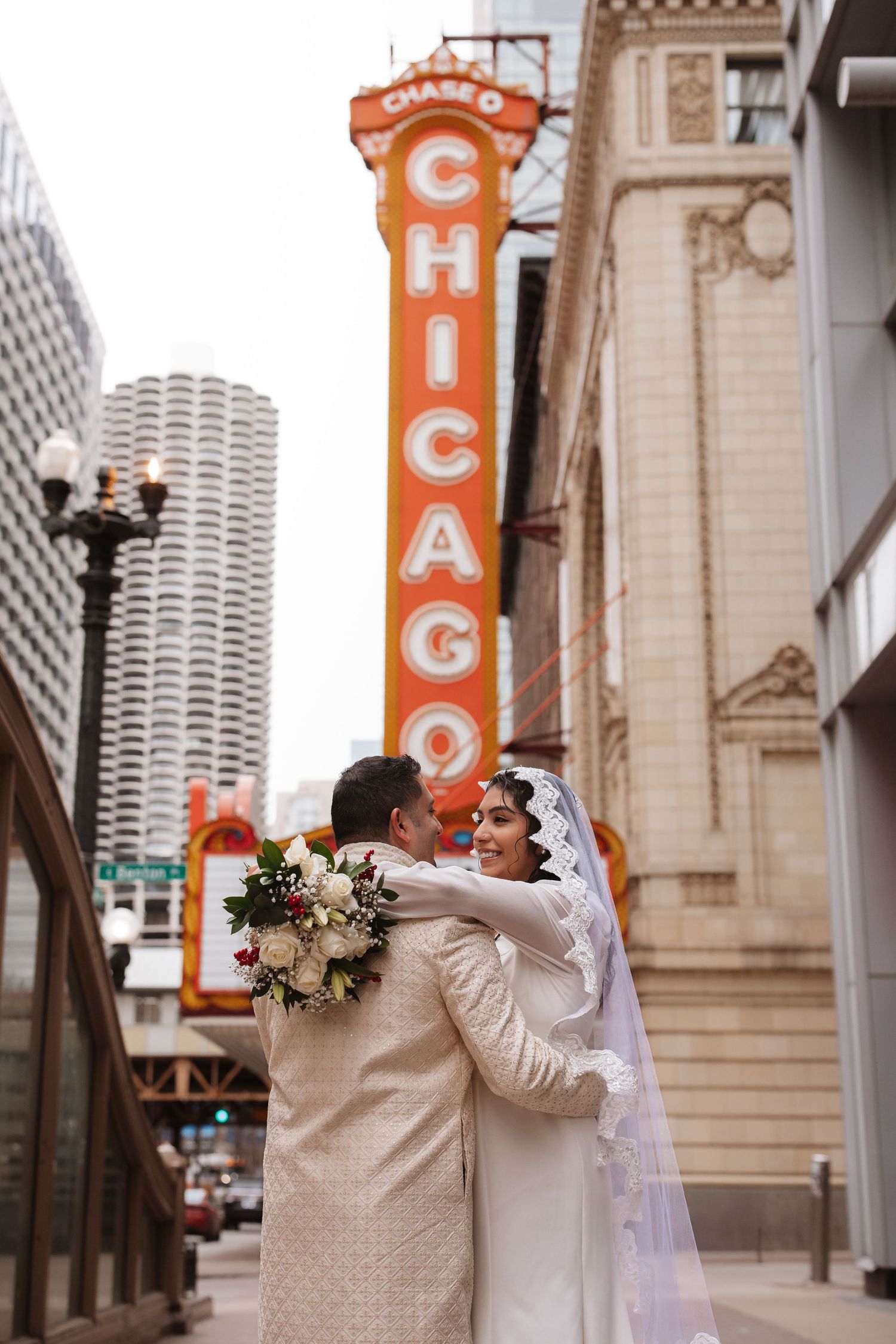Newlyweds embrace romantically in front of the glowing Chicago Theatre sign on State Street.