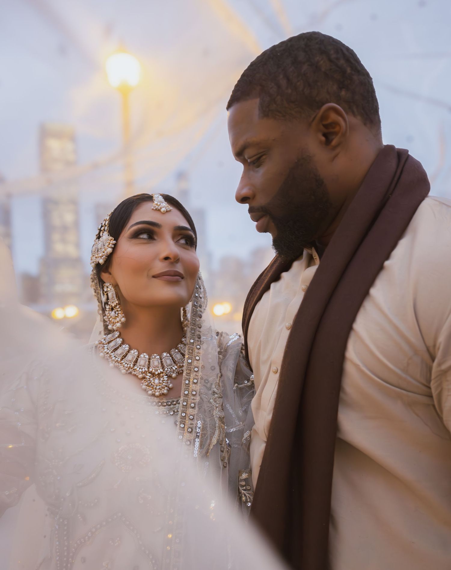 Close-up of South Asian bride in kundan jewelry and groom in cream sherwani gazing at each other.