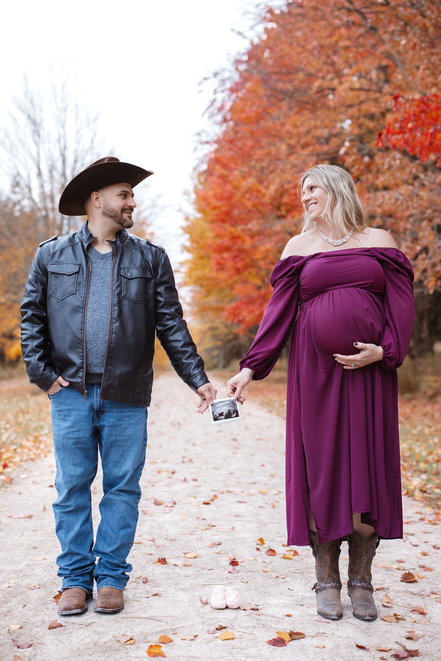 Happy expecting couple holding ultrasound photo together on scenic autumn tree-lined path.