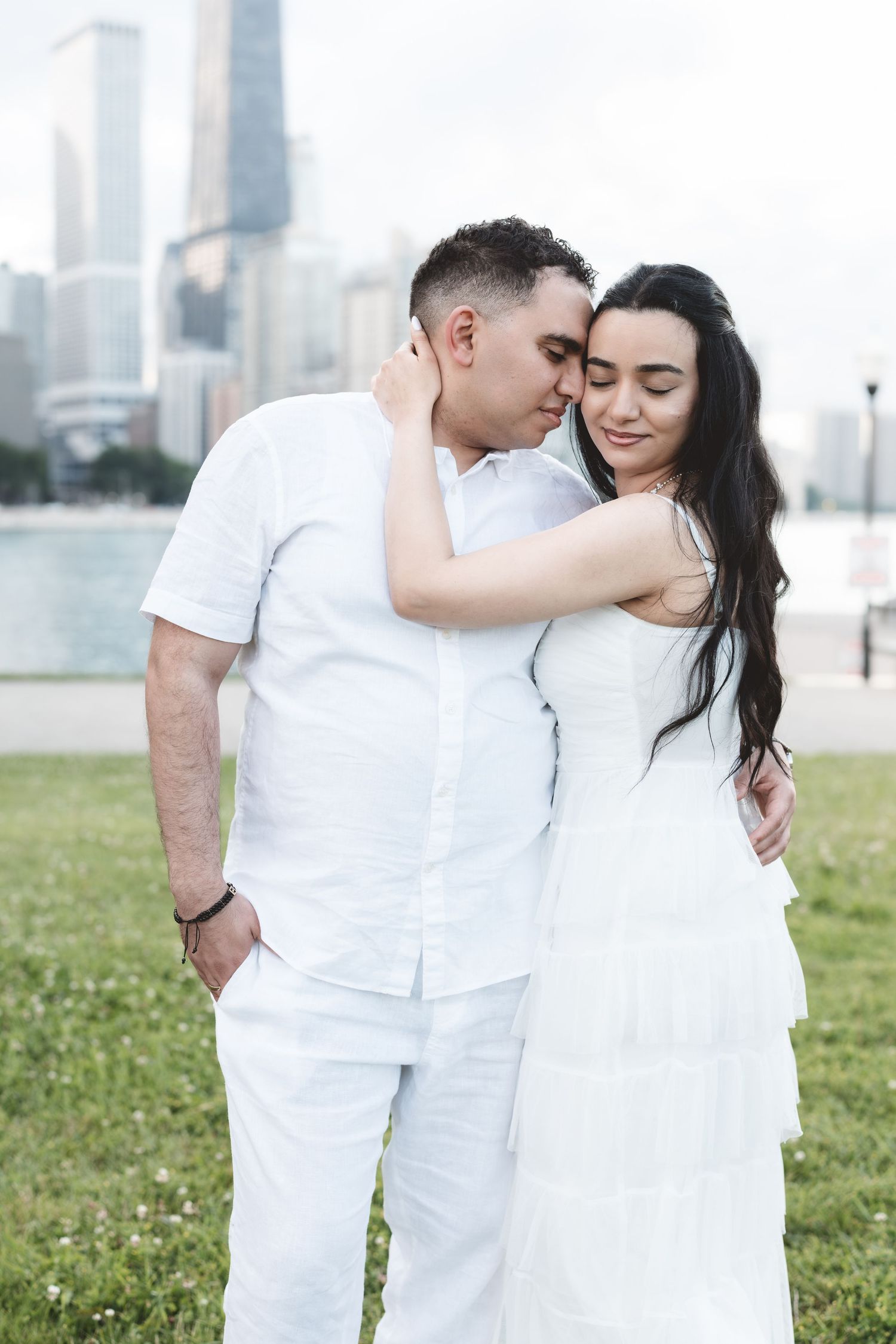A romantic couple in white embracing tenderly with the Chicago skyline behind them.