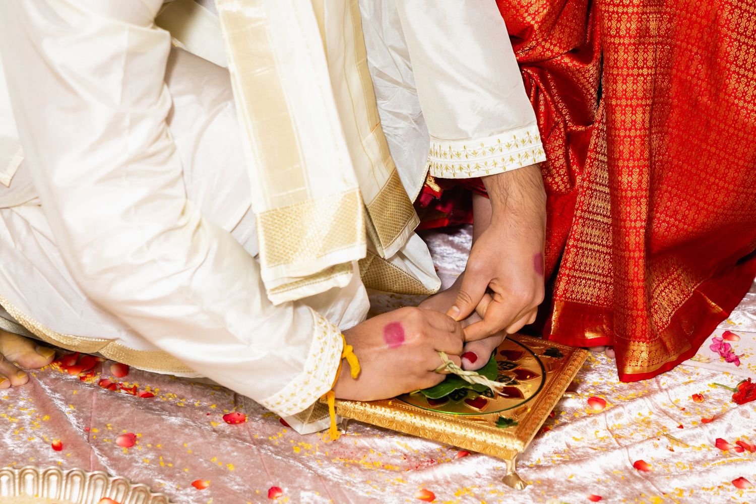 Hindu bride and groom exchanging hands during traditional wedding ritual with rose petals on ornate cloth.