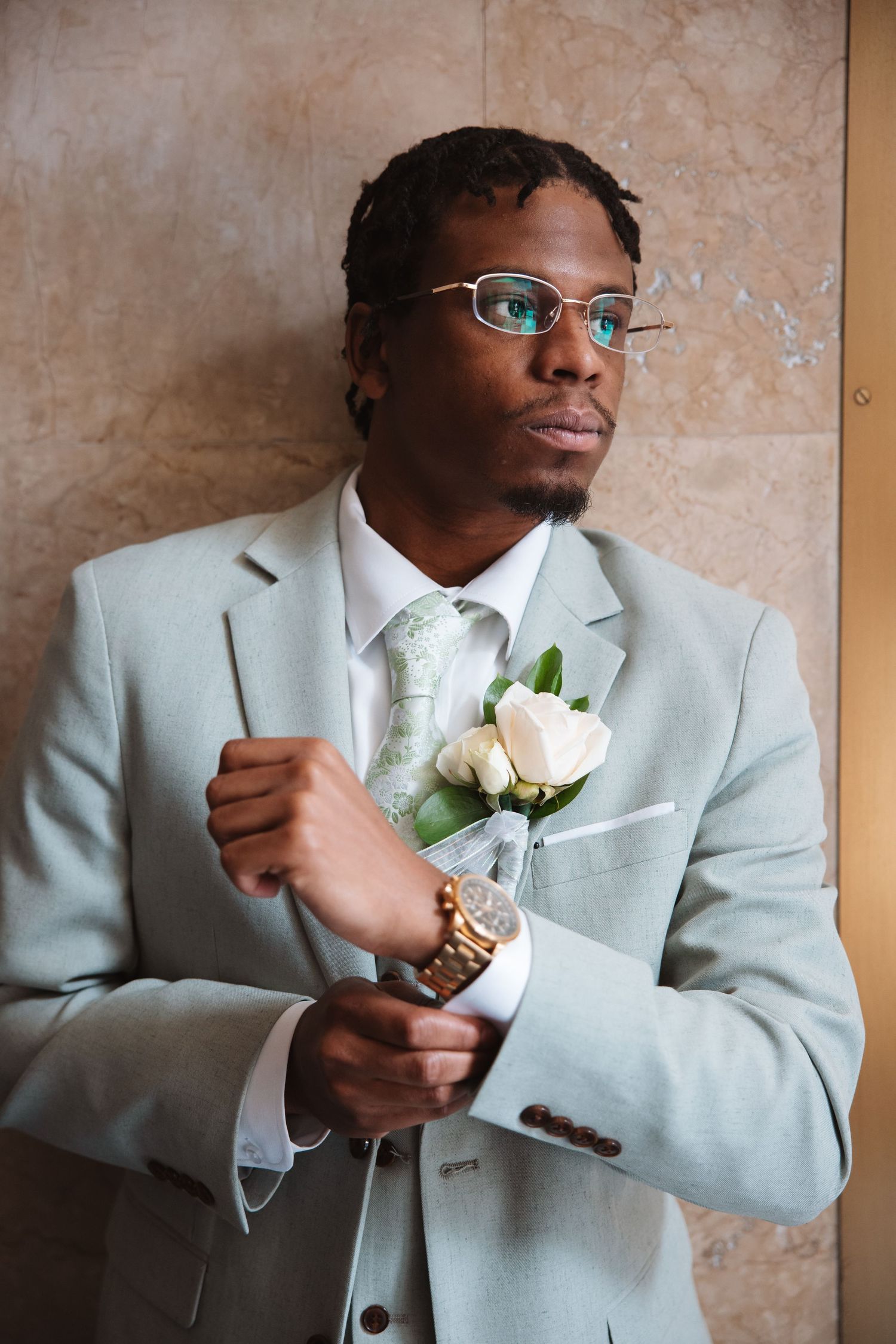 Groom in light gray suit adjusting cufflinks with boutonniere and gold watch.