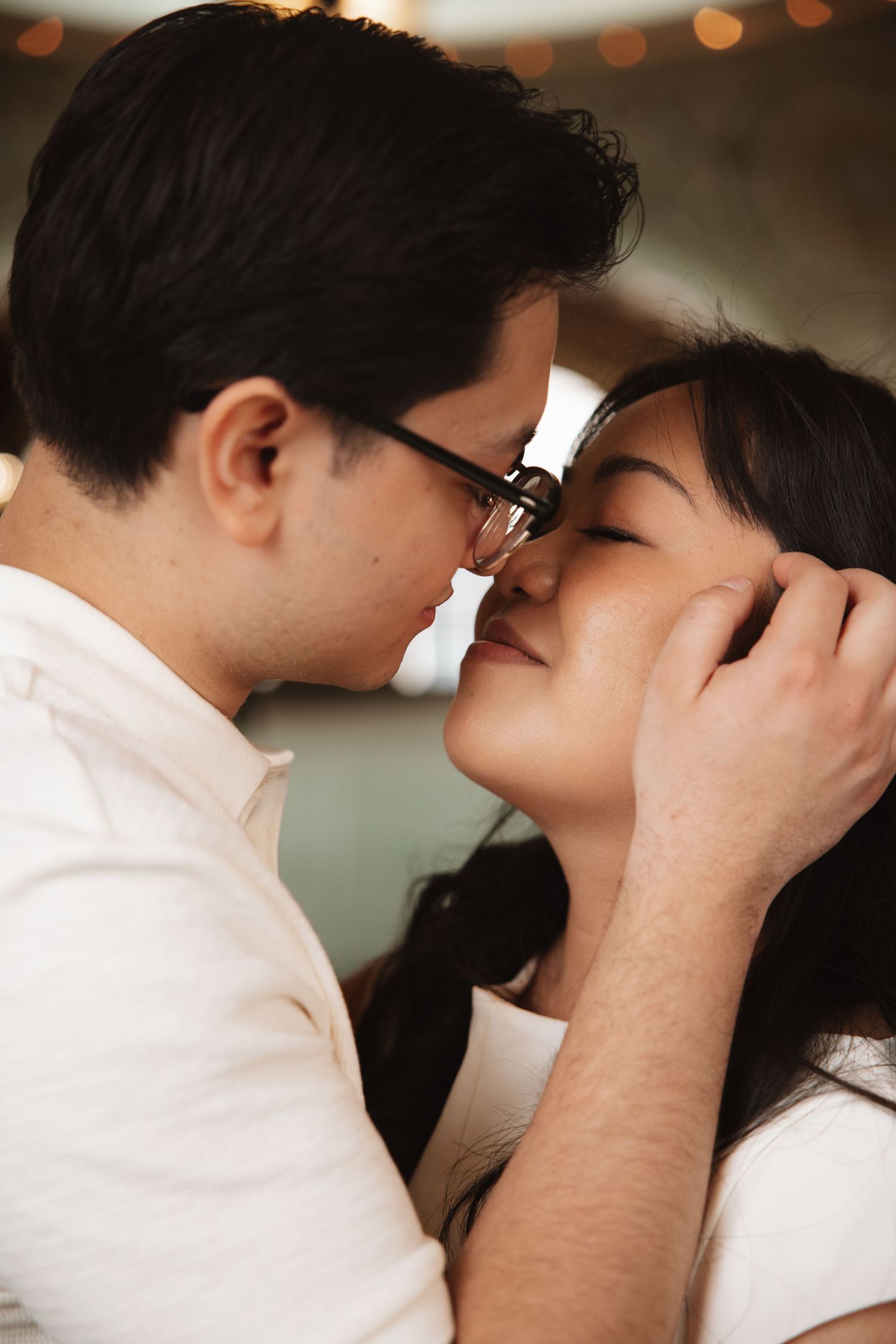 Close-up of couple sharing a tender almost-kiss, man holding woman's face gently with warm bokeh background.