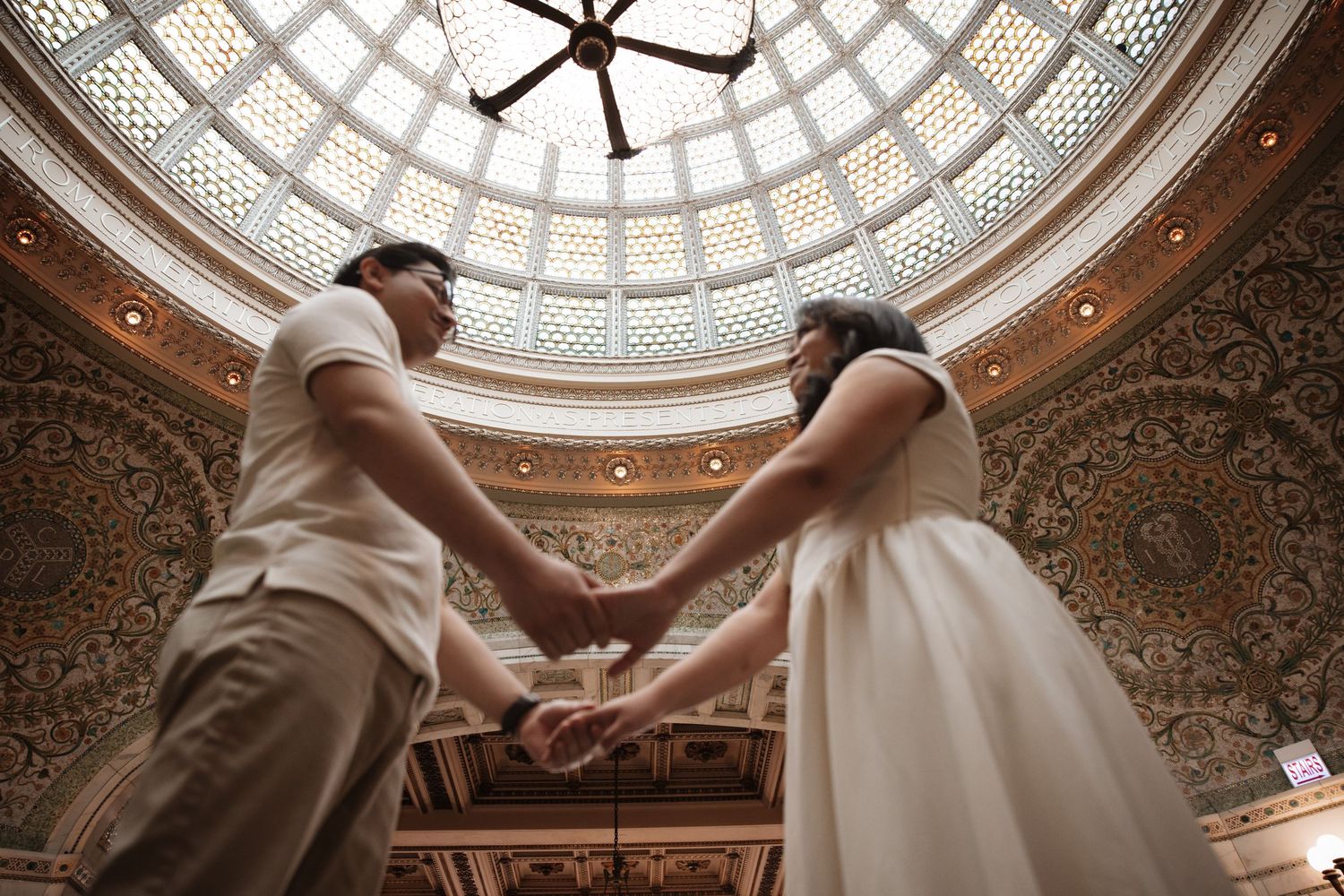 Couple holds hands beneath the stunning ornate mosaic dome of the Chicago Cultural Center.