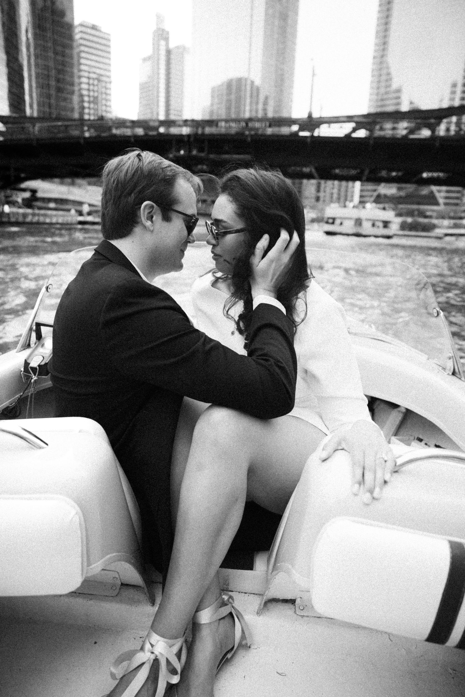 Black and white photo of couple almost kissing on a vintage boat with Chicago city skyline in background.