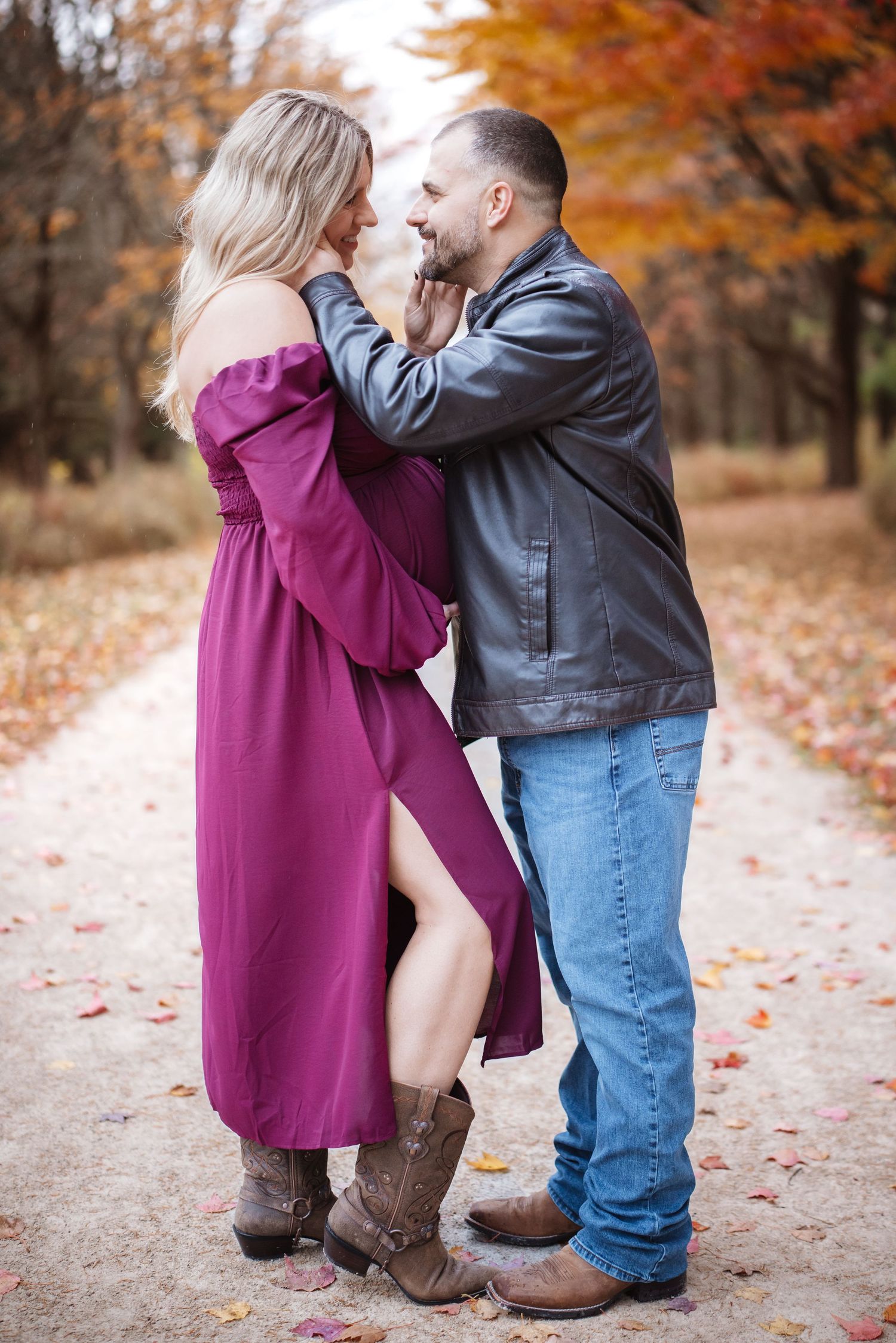 Smiling couple in autumn park, woman in purple off-shoulder maternity dress with cowboy boots and man in leather jacket and jeans.