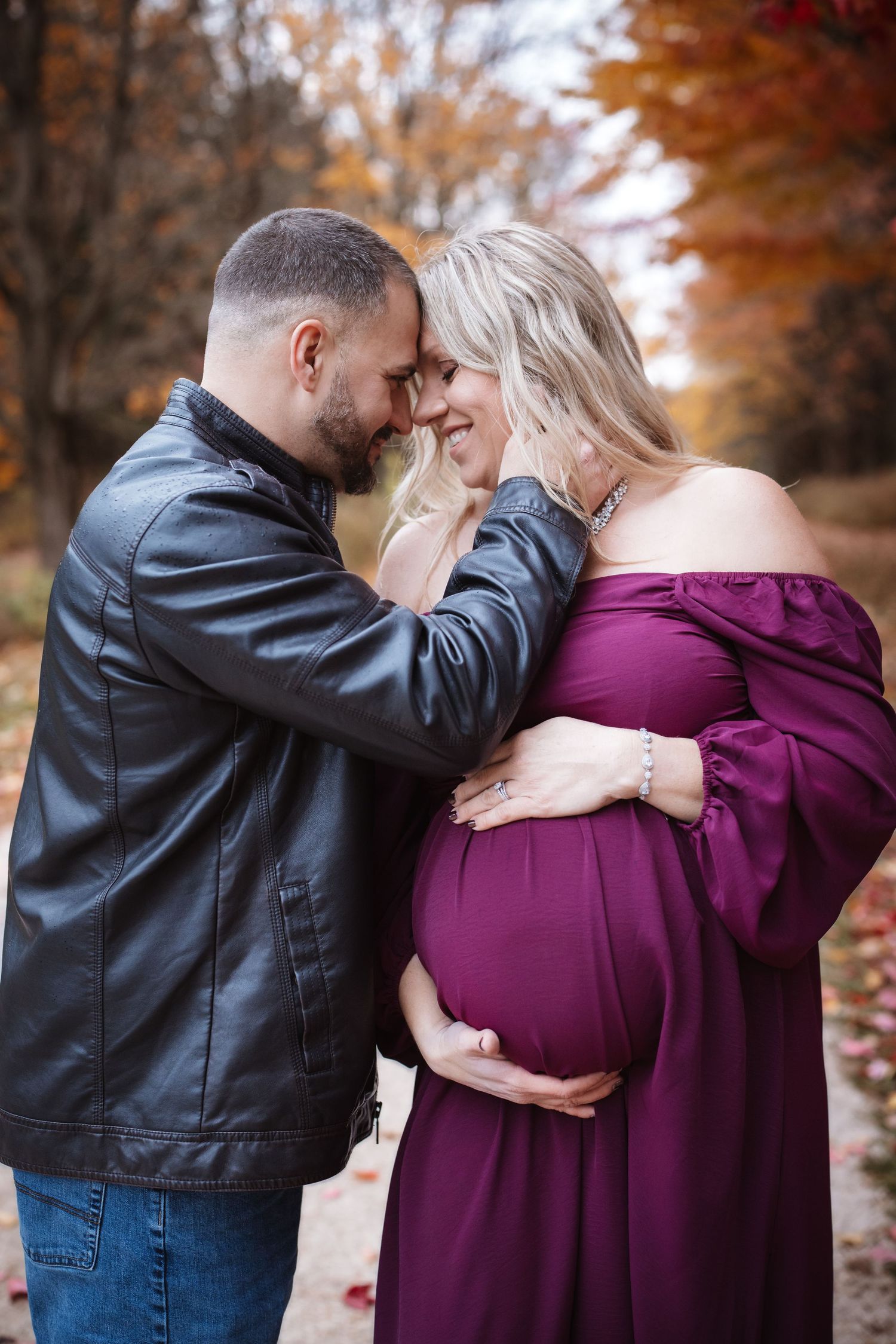 Happy expecting couple sharing intimate forehead touch during colorful autumn maternity shoot.