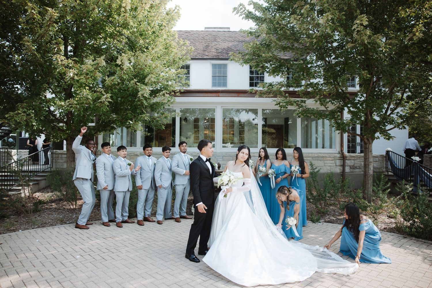 Bride and groom share romantic moment as wedding party celebrates around them on brick patio.