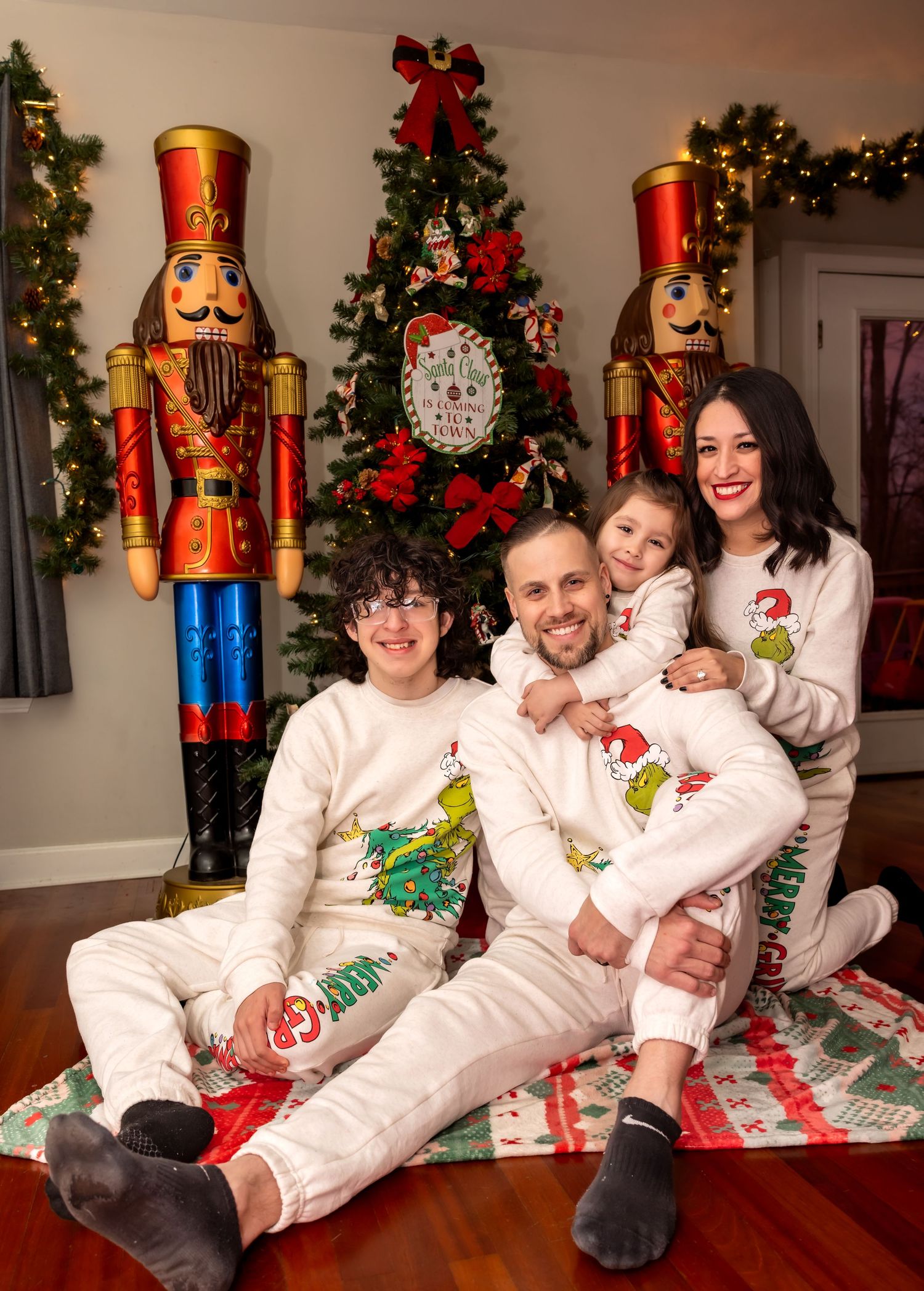 Family of four wearing matching Grinch Christmas pajamas posing in front of a decorated holiday tree.
