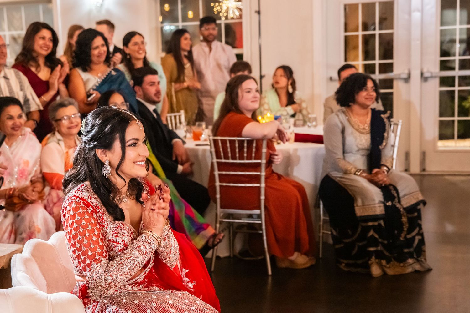 Bride in red lehenga with mehndi hands clasped at wedding reception.