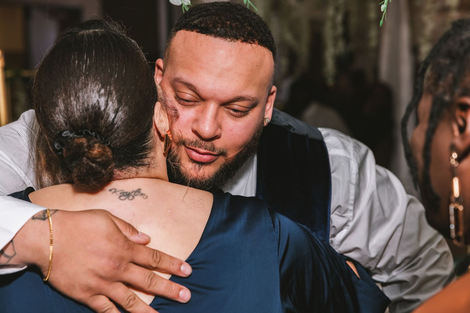 Man in grey shirt giving a heartfelt hug to a woman at a wedding.