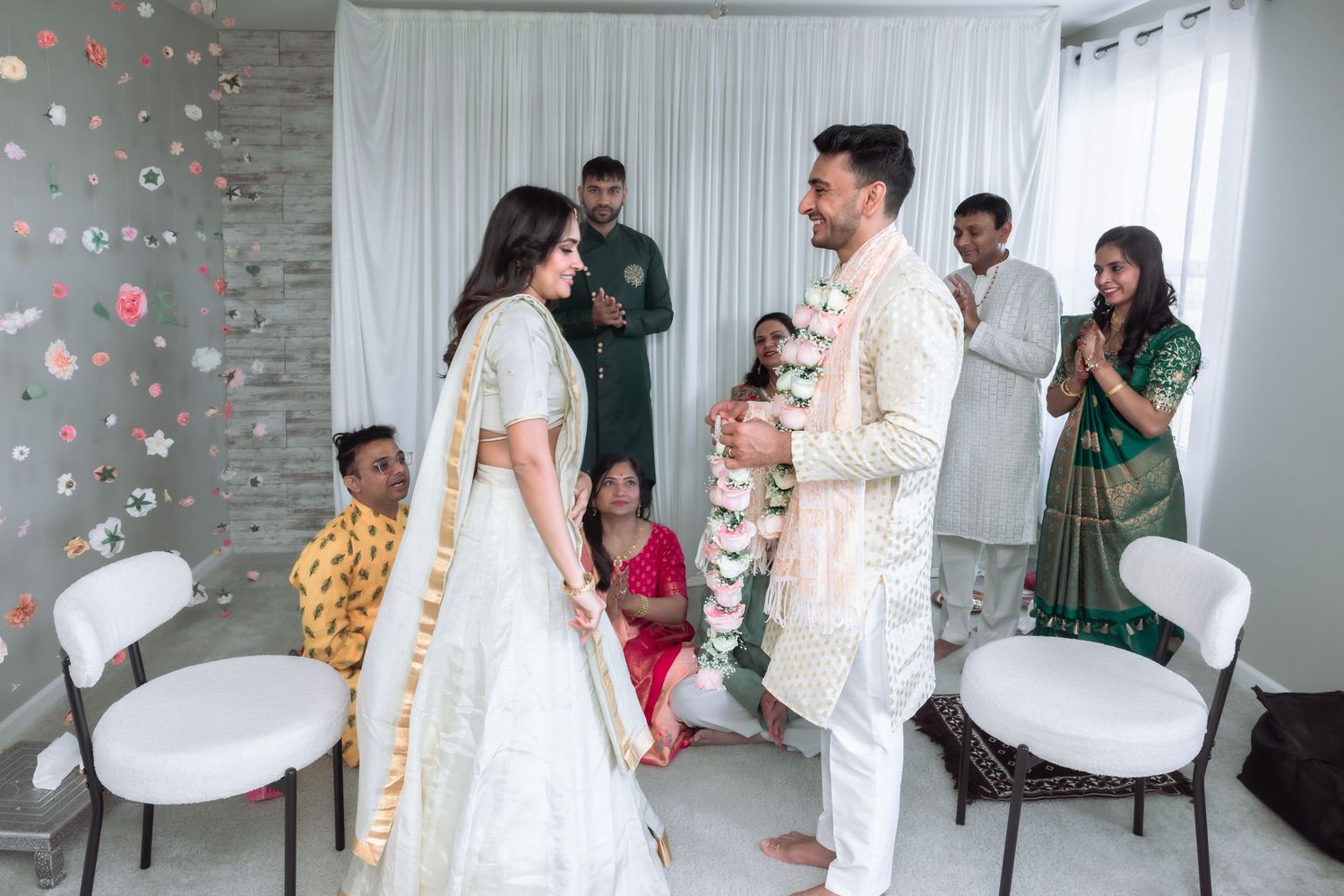 Bride and groom exchange floral garlands during a traditional Indian Varmala wedding ceremony indoors.