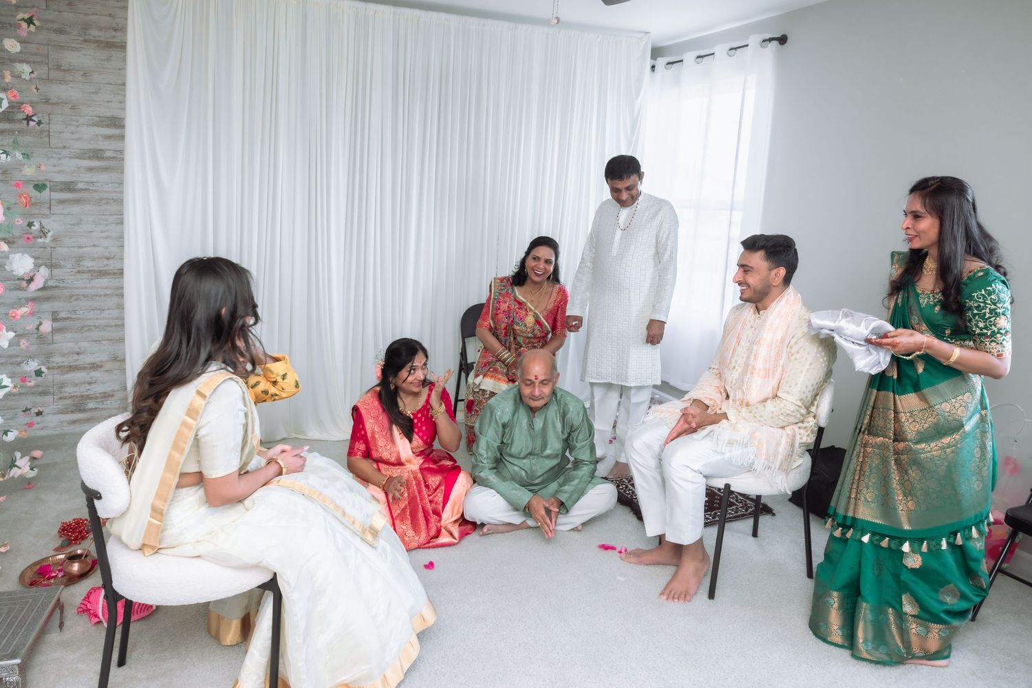 Family members dressed in colorful Indian traditional wear participate in a pre-wedding ceremony indoors.