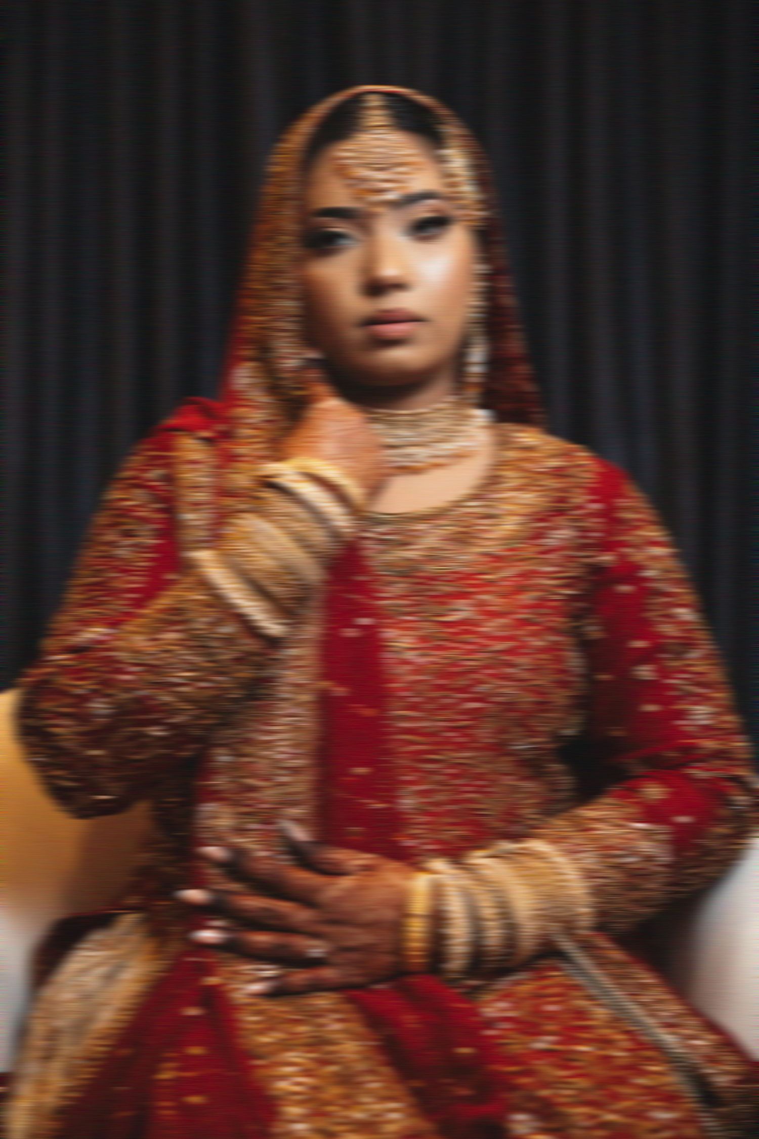 A softly blurred portrait of an Indian bride in traditional red and gold wedding attire and jewelry.