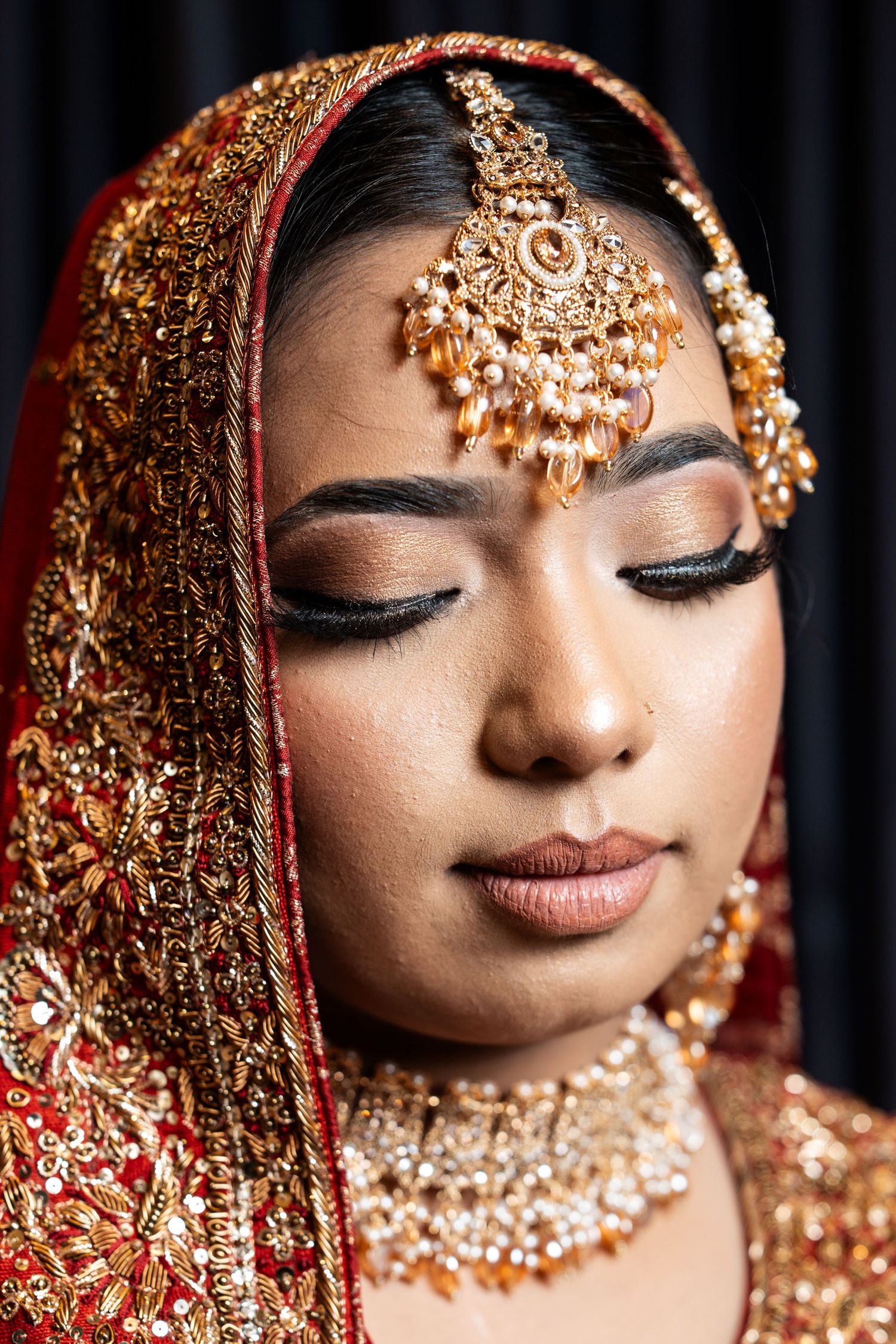 Close-up of a bride wearing an ornate gold maang tikka and traditional Indian bridal jewelry.