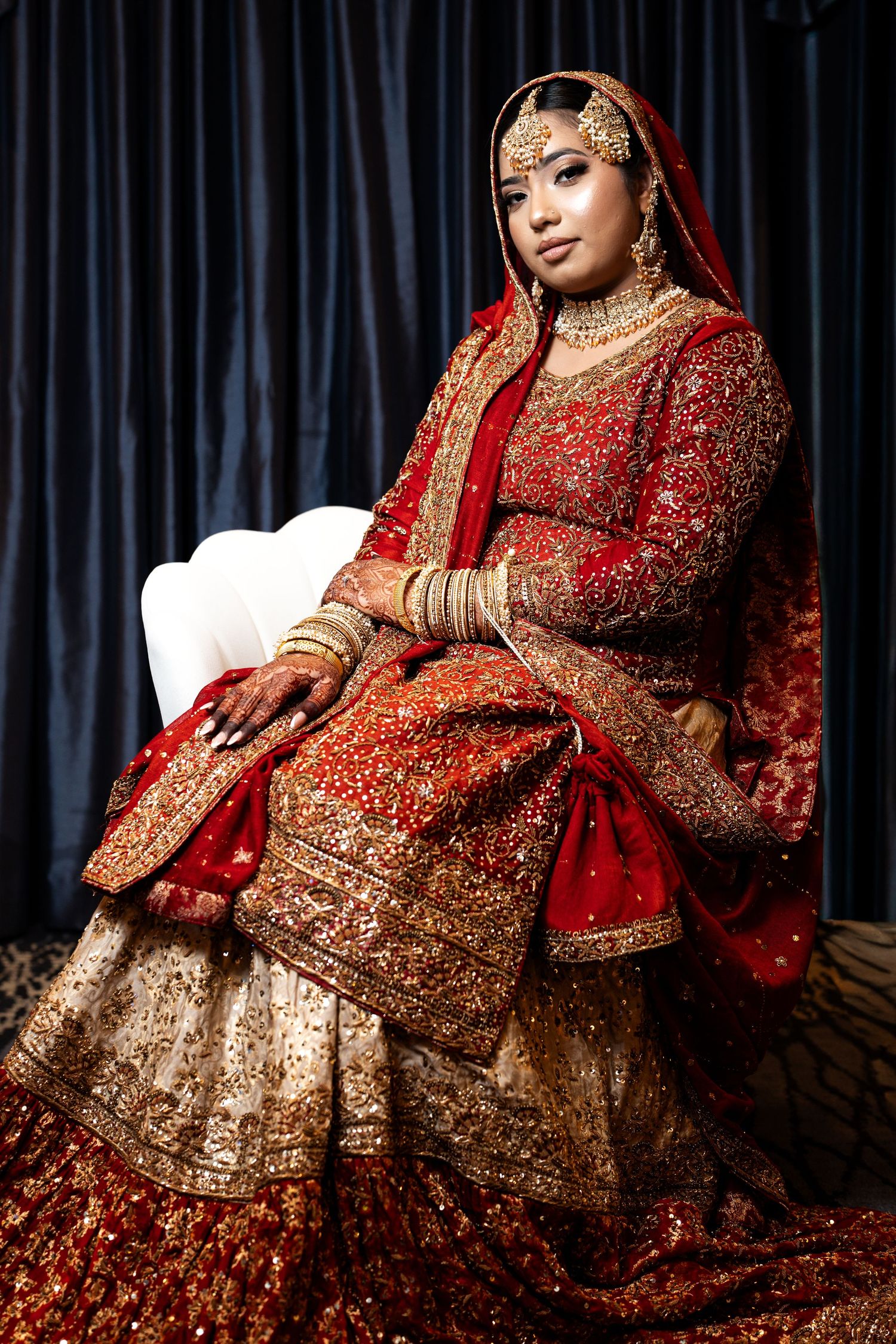 Bride in stunning red and gold embroidered South Asian bridal outfit with gold jewelry.