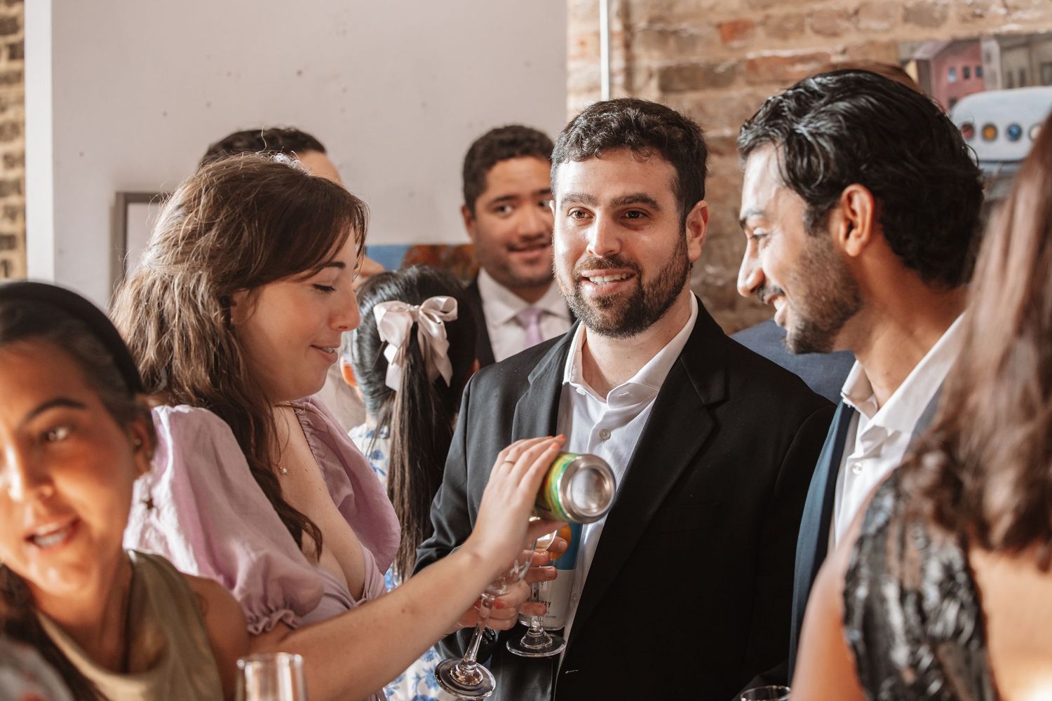 Friends laughing and socializing with drinks at a lively indoor social gathering.