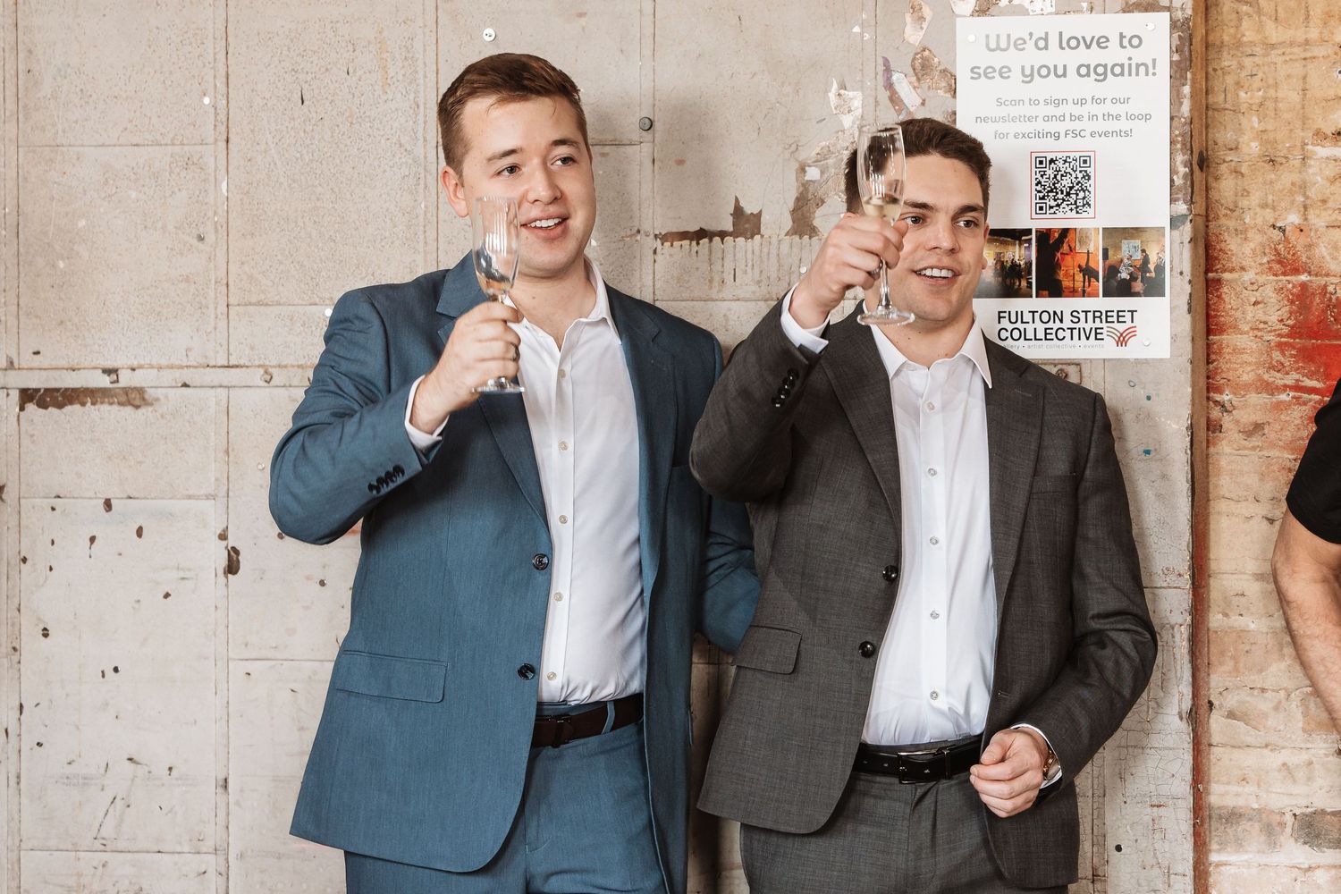 Two young men in suits toasting with champagne glasses at a formal event.