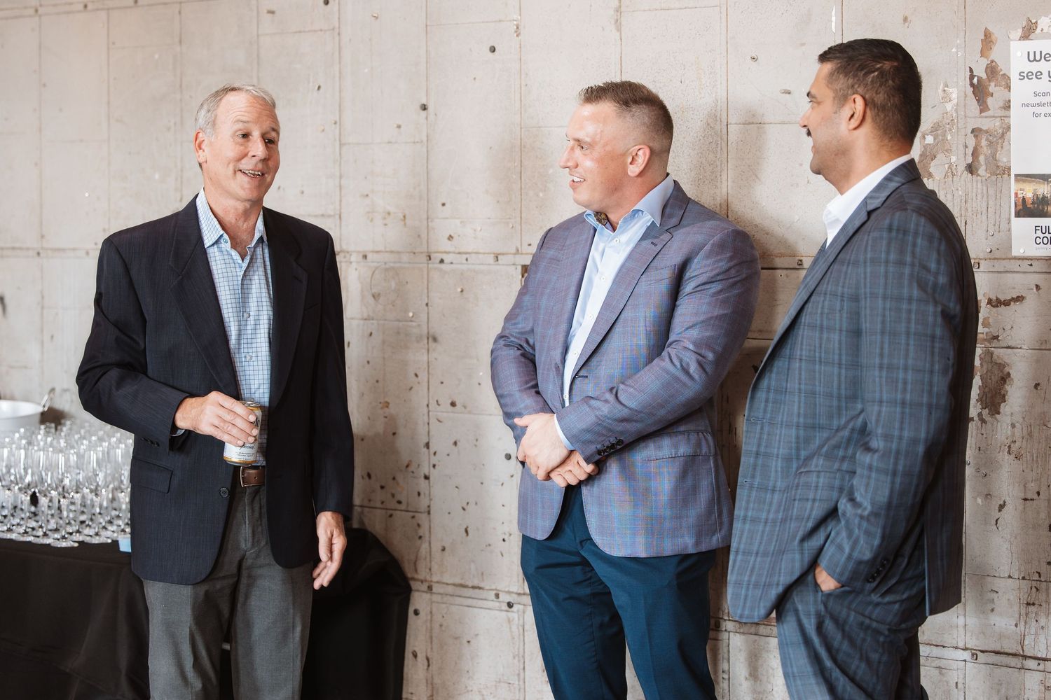 Three men in business attire networking and conversing at a professional event.
