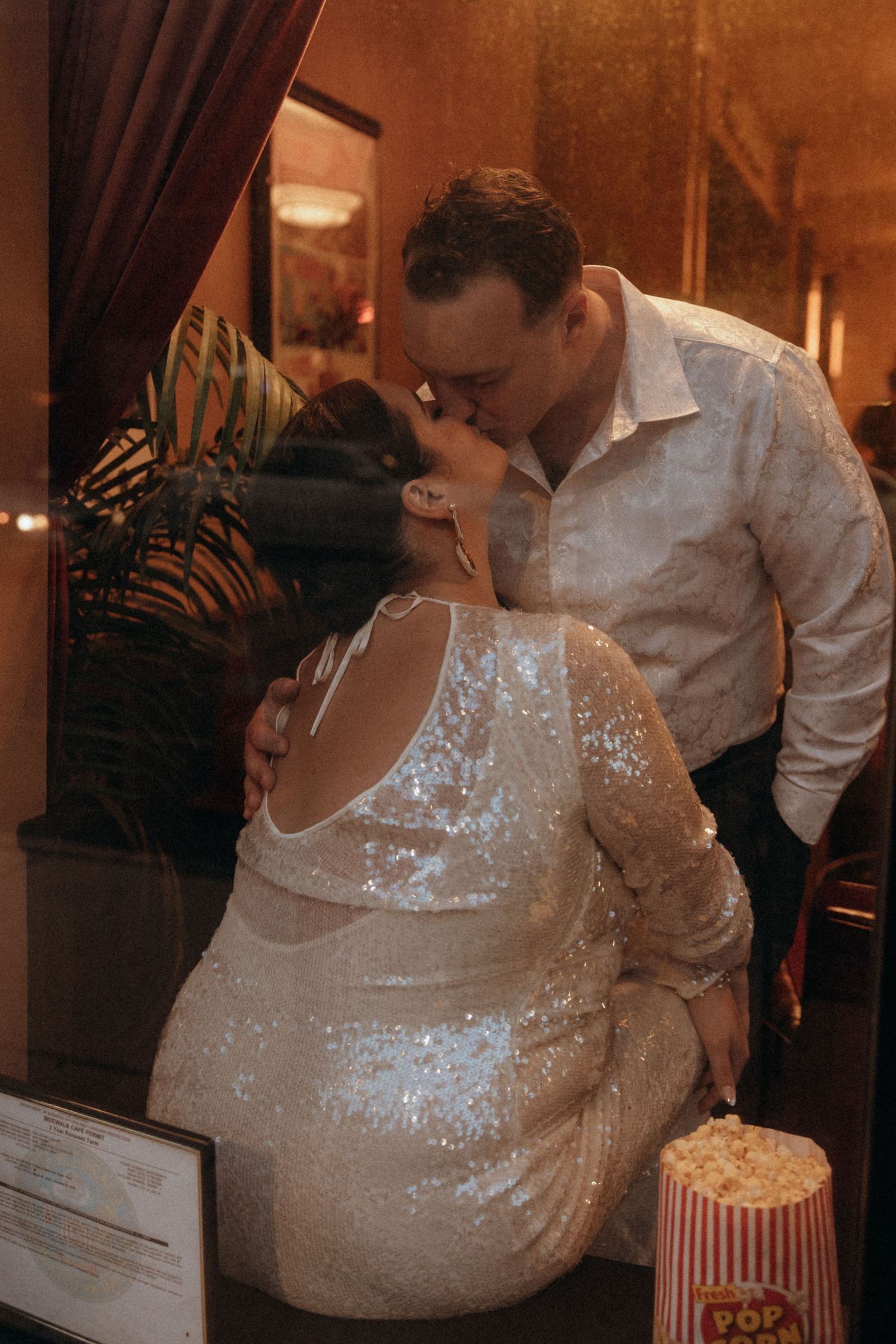 Bride and groom share a kiss near a popcorn stand in a warmly lit wedding venue.