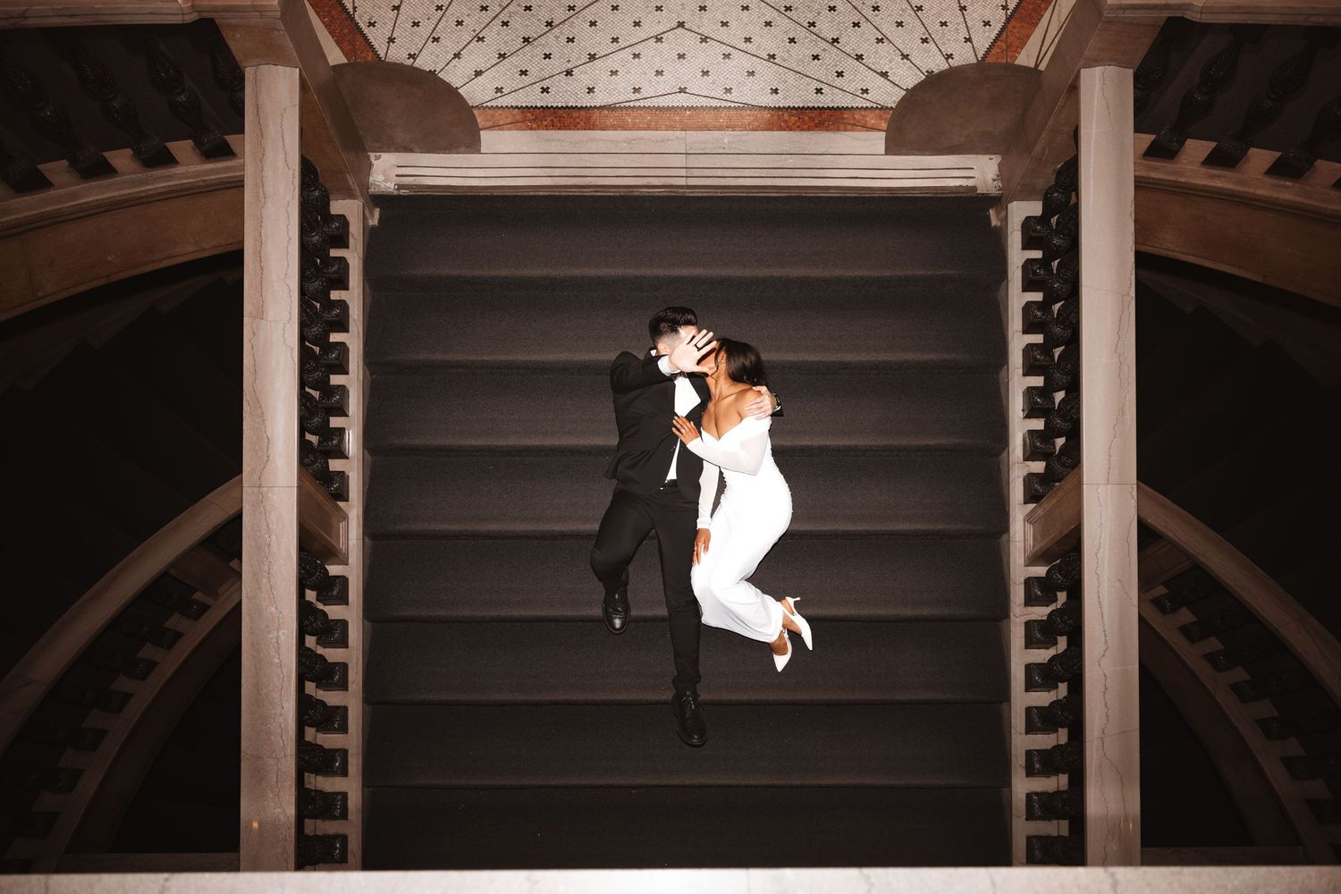 Top-down view of newlyweds kissing on ornate staircase in stunning wedding attire.Chicago Wedding Photographer