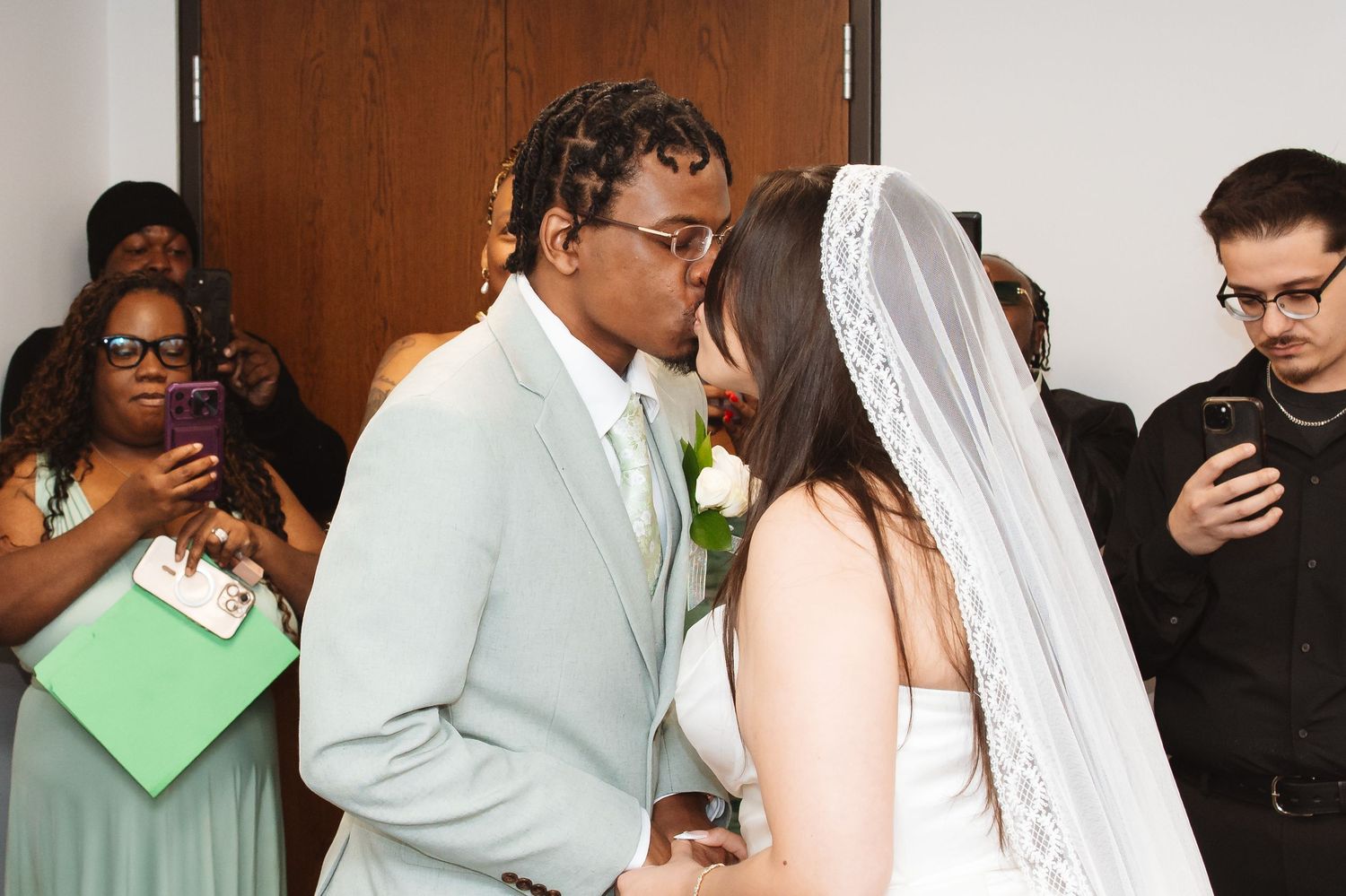A couple shares their first kiss at the altar during a wedding ceremony, surrounded by guests capturing the moment.